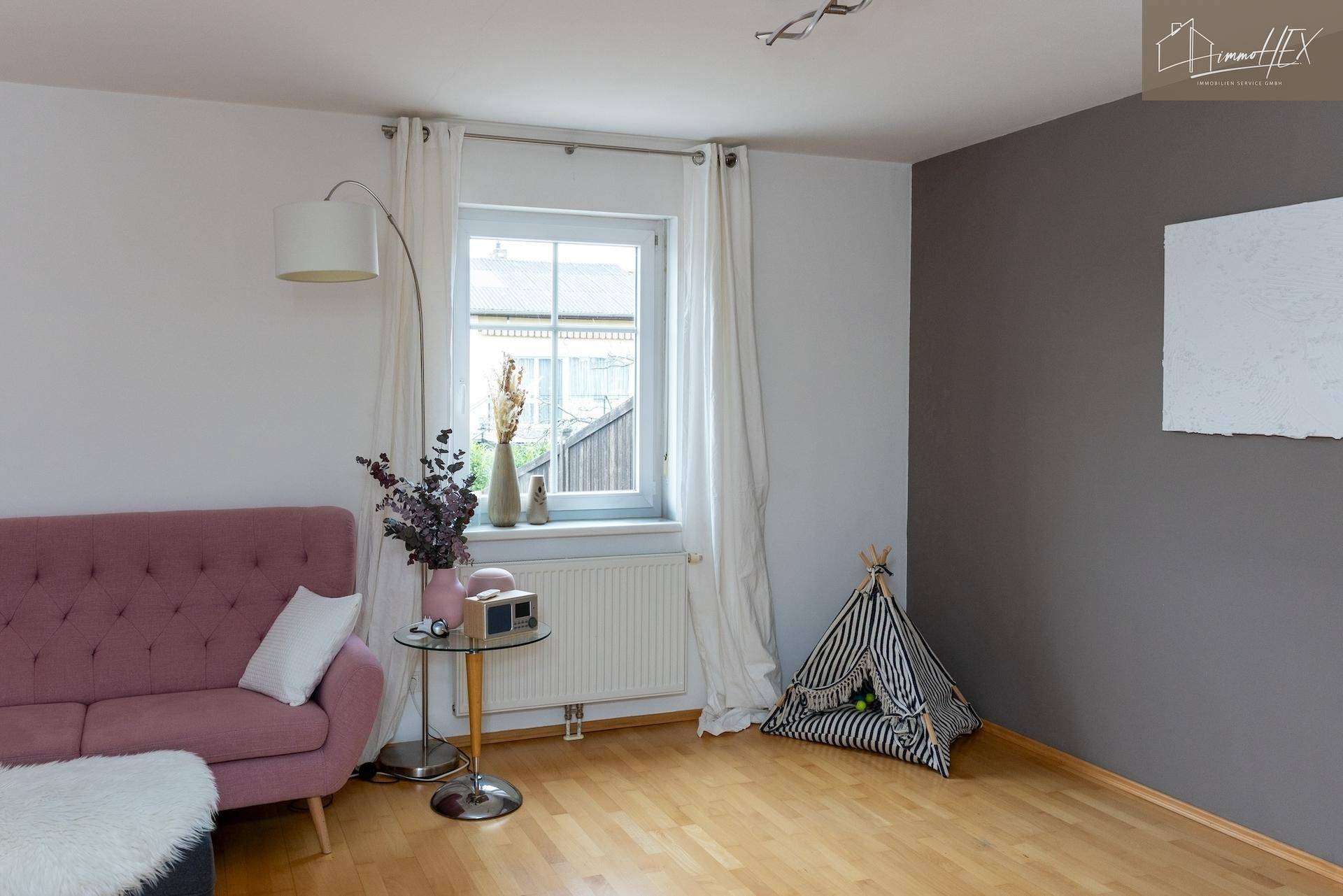 Gemütliche Ecke im Wohnzimmer mit rosa Sofa, Fenster und Holzboden.