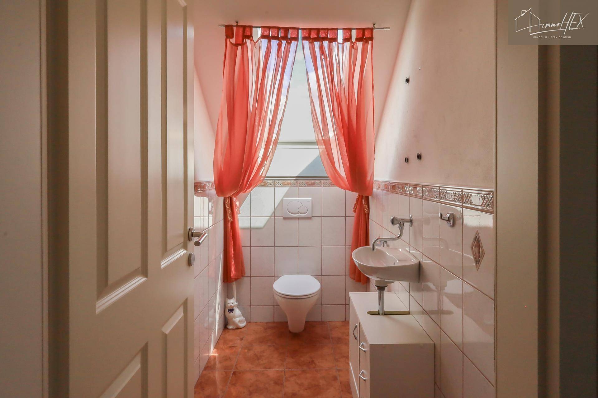 Kleines Gäste-WC mit Fenster, Fliesenboden und auffälligen roten Vorhängen.
