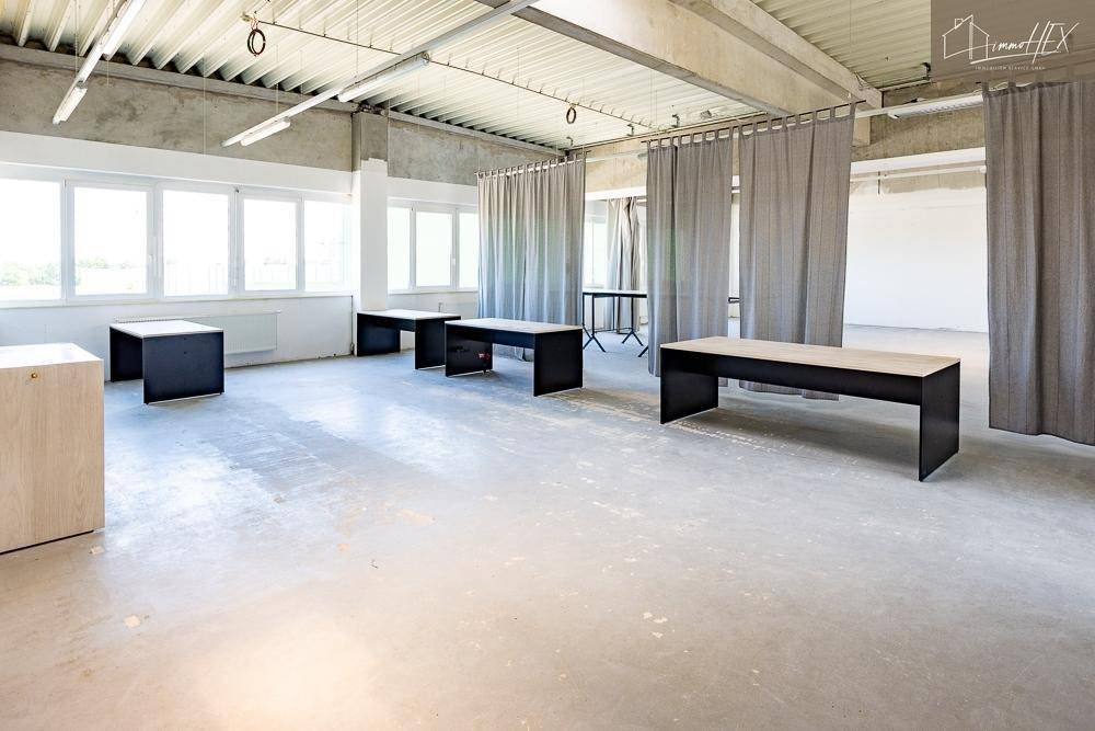 Heller Bürobereich mit großen Fenstern, die viel Licht hereinlassen, und einem robusten Betonboden.