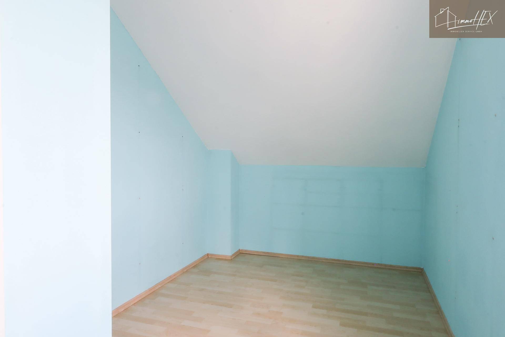Leeres Dachzimmer mit hellblauen Wänden und hellem Laminatboden, bereit zur individuellen Gestaltung.