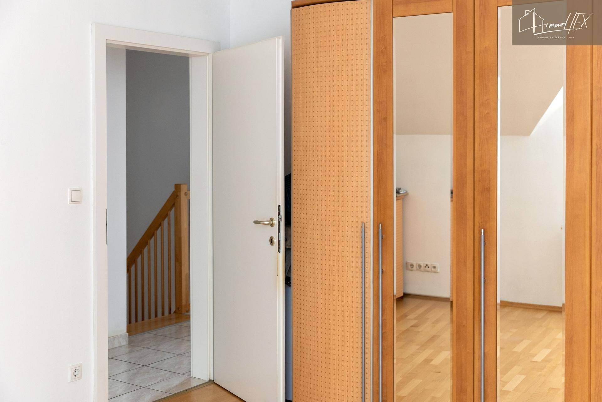 Zimmer mit Holzboden, weißen Wänden und einem großen Holzschrank mit Spiegeltüren.