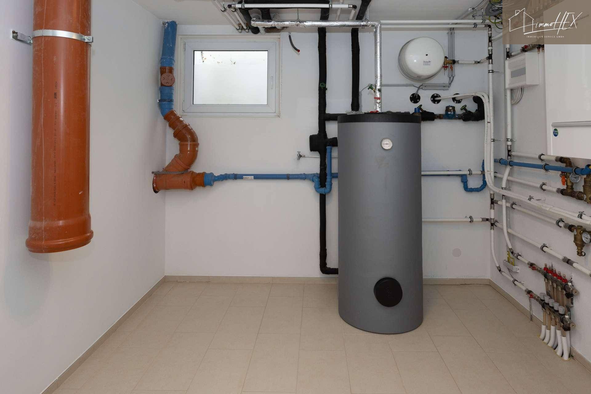 Technikraum mit zentralem Warmwasserspeicher und umfangreicher Rohrinstallation.