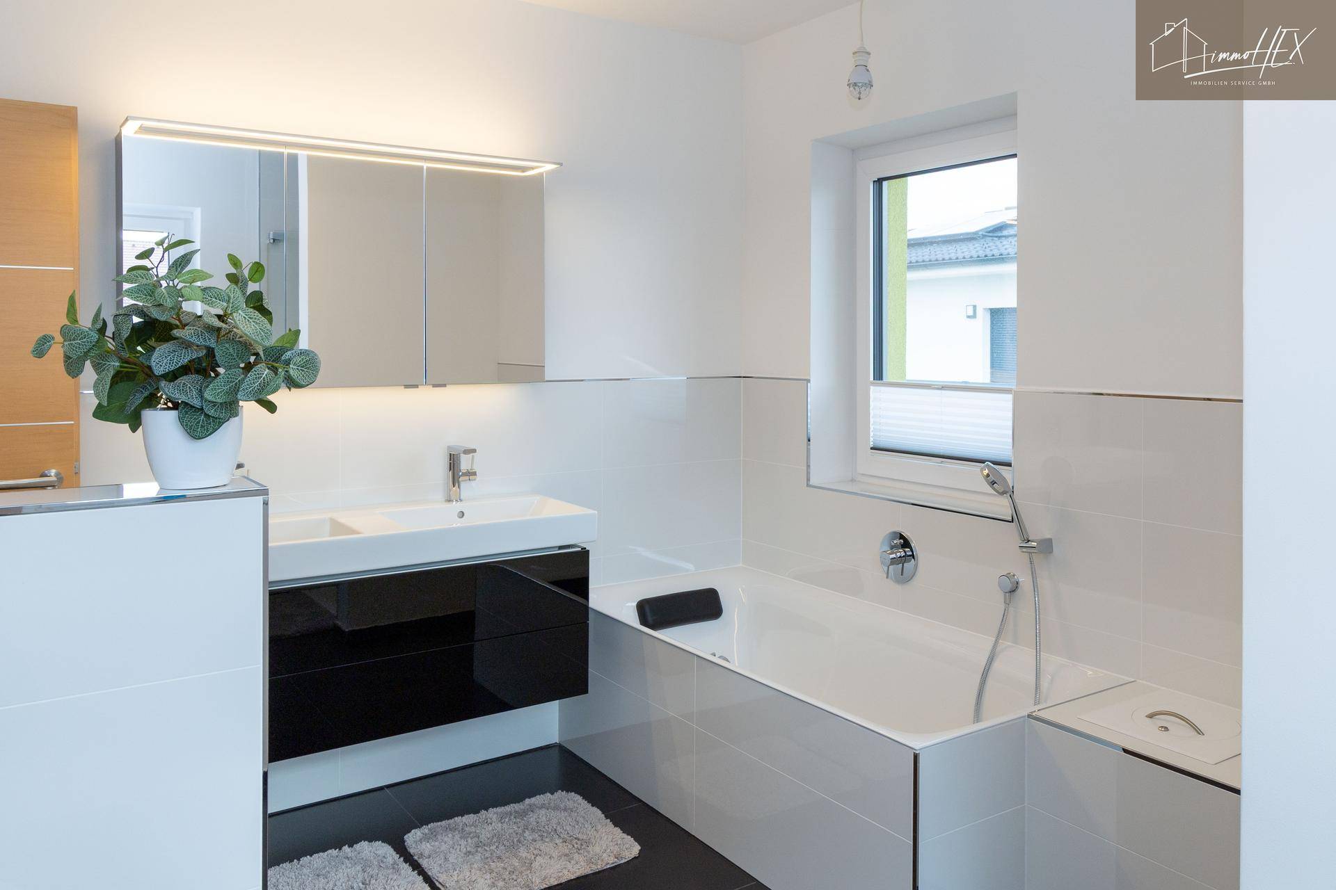 Modernes Badezimmer mit Doppelwaschbecken, beleuchtetem Spiegelschrank und Badewanne.