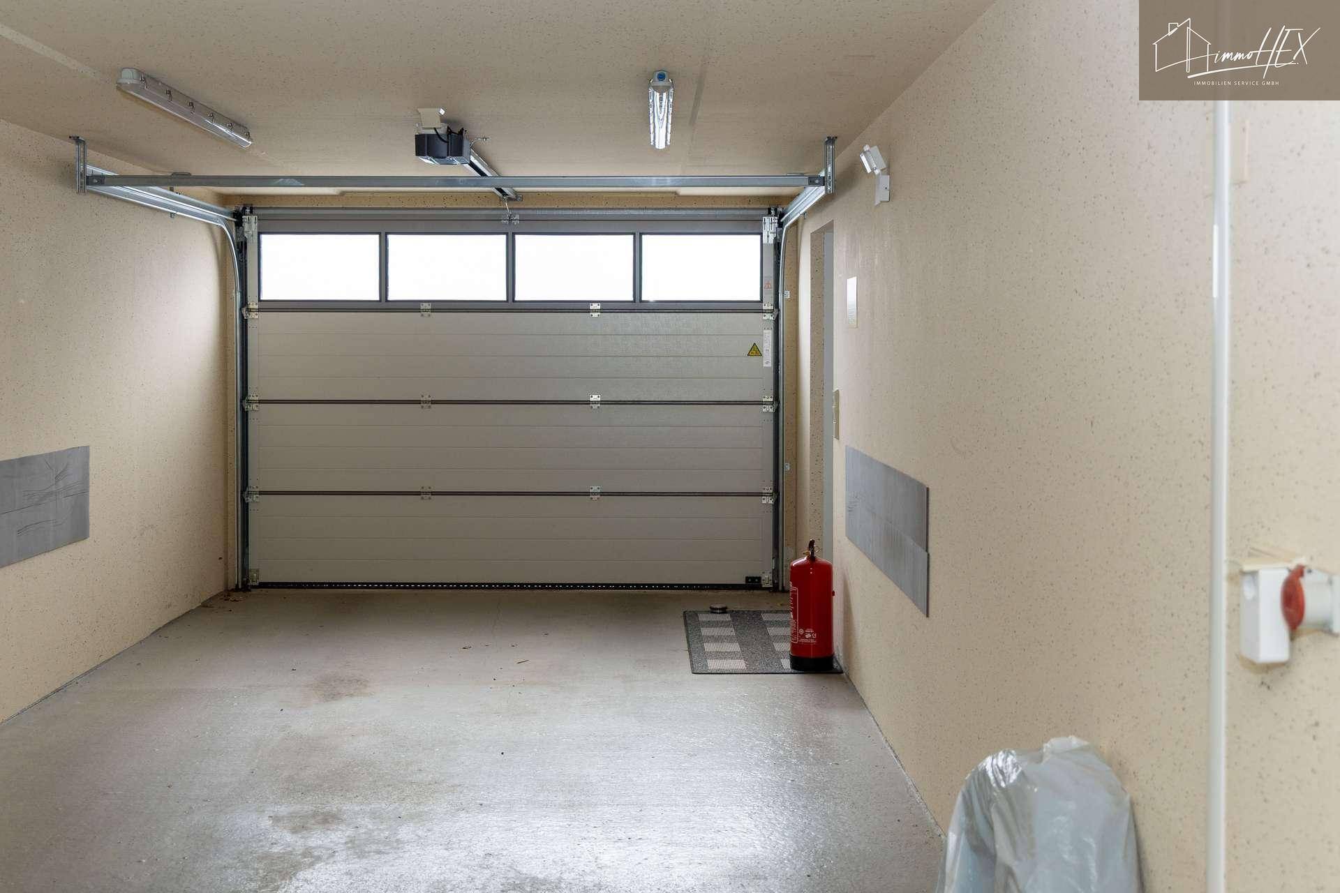 Geräumige Garage mit automatischem Tor und Betonboden, bietet Platz für ein Fahrzeug.