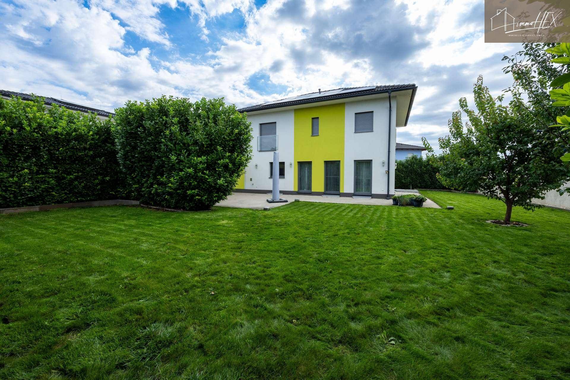 Rückansicht des Hauses mit weitläufigem Rasen und hohen Hecken, bietet Privatsphäre.