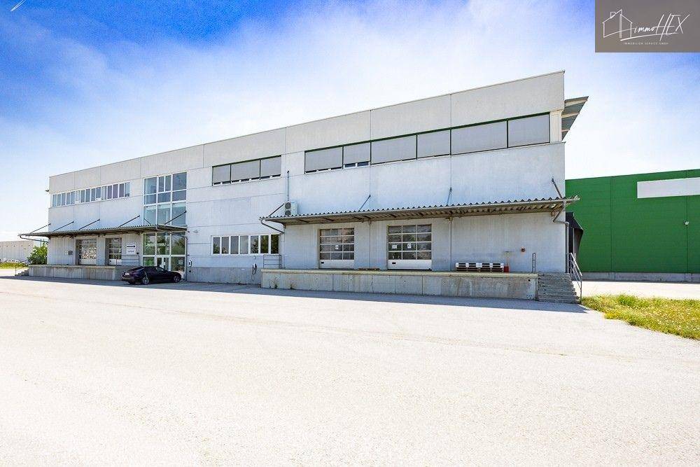 Modernes Industriegebäude mit weißer Fassade, großen Fensterfronten und weitläufigem Parkplatz.