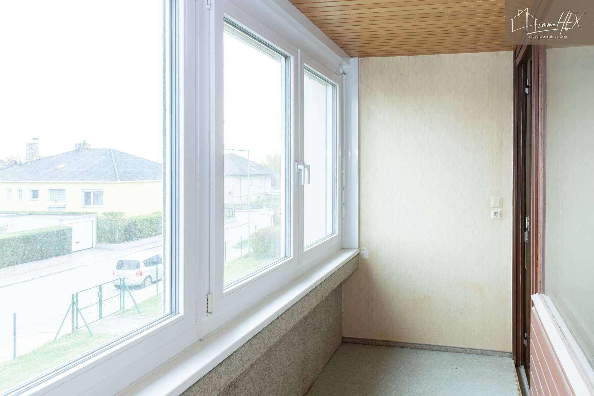 Helle Loggia mit großen Fenstern und Blick auf die umliegenden Häuser und die Straße.