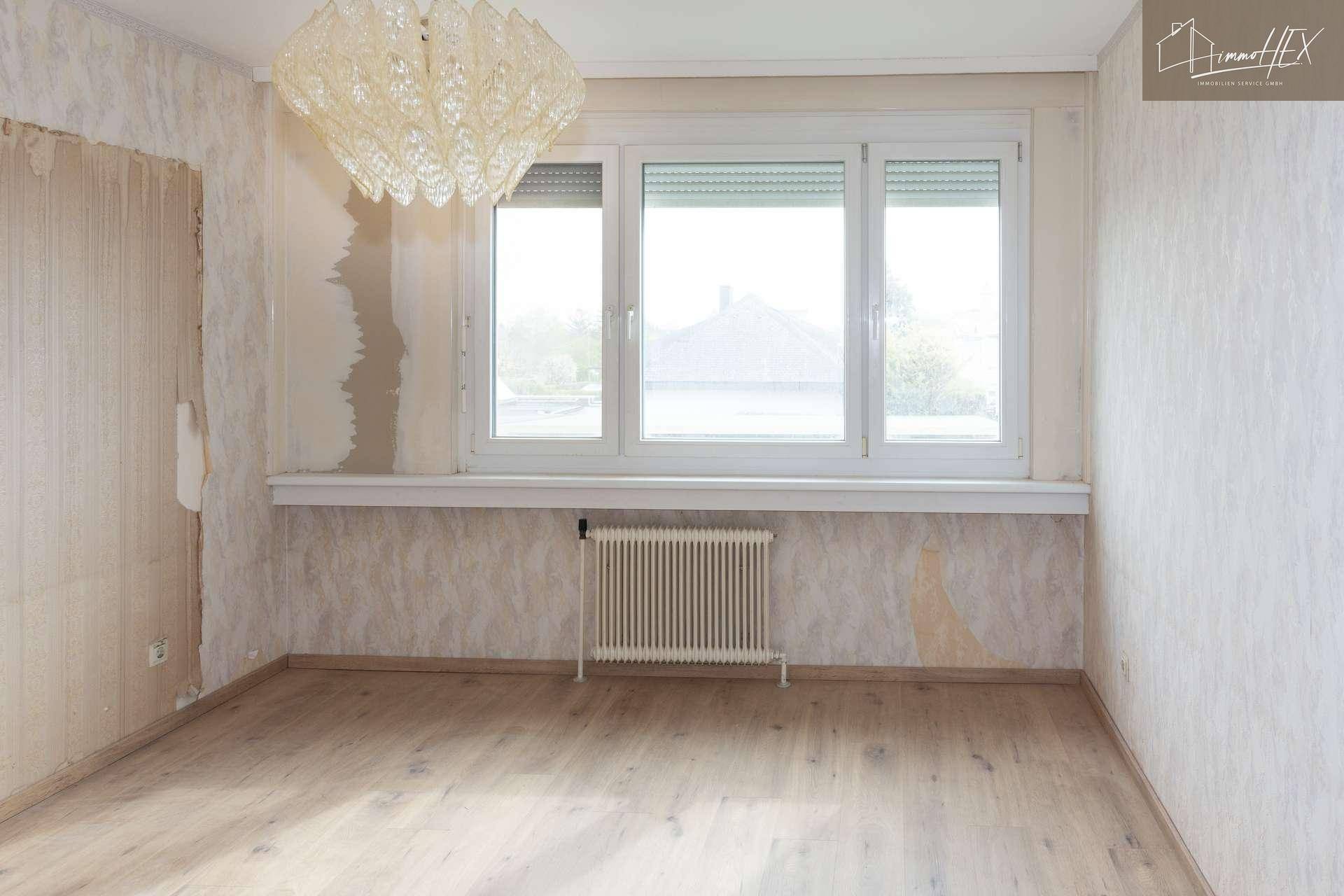 Geräumiges Schlafzimmer mit abgelöster Tapete und hellen Fenstern, die auf die Umgebung blicken.