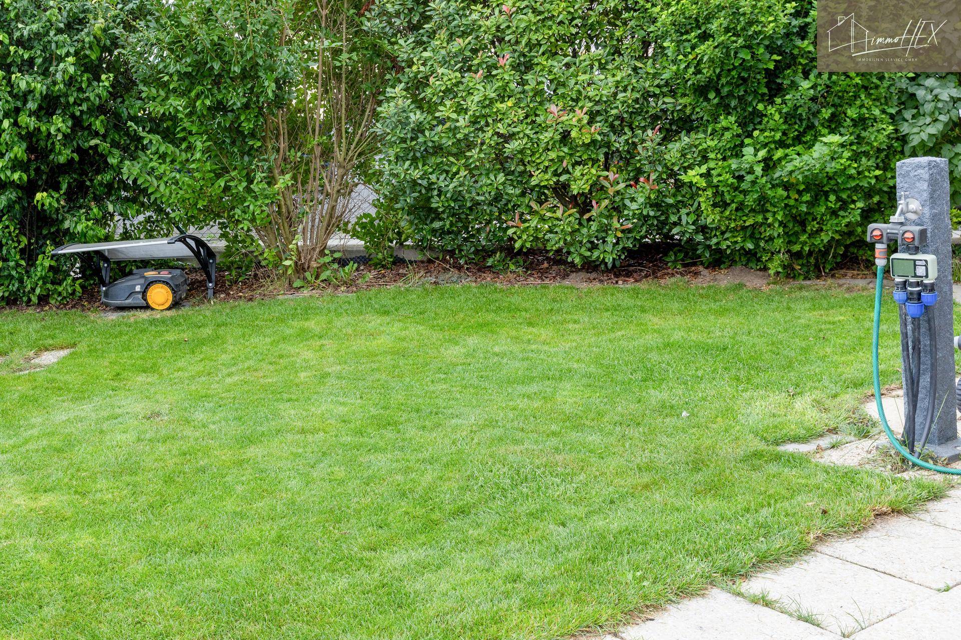 Grüner Garten mit Rasenfläche und automatischem Rasenmäher, gut gepflegt.