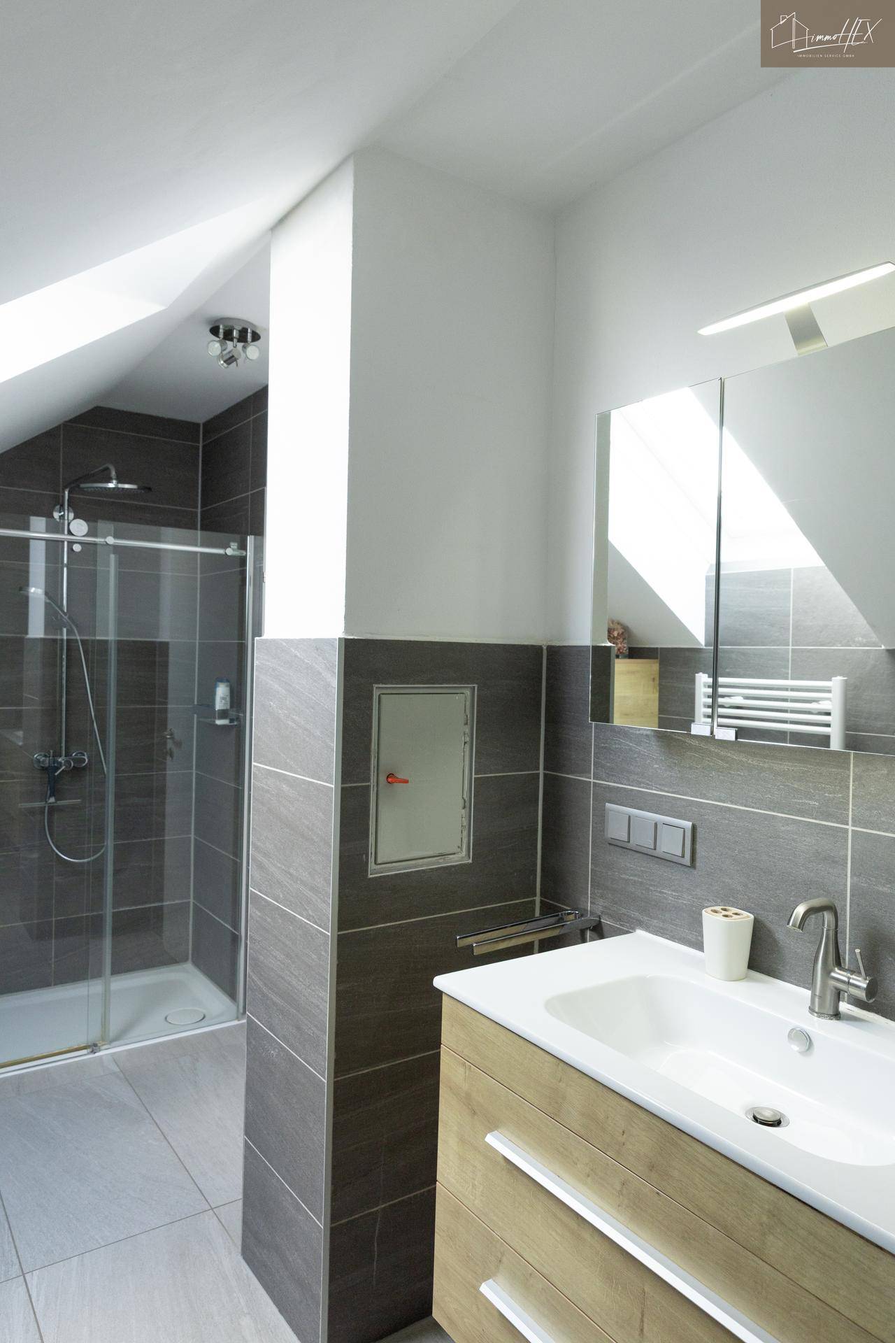 Modernes Badezimmer mit Dusche, Waschbecken und grauen Fliesen.