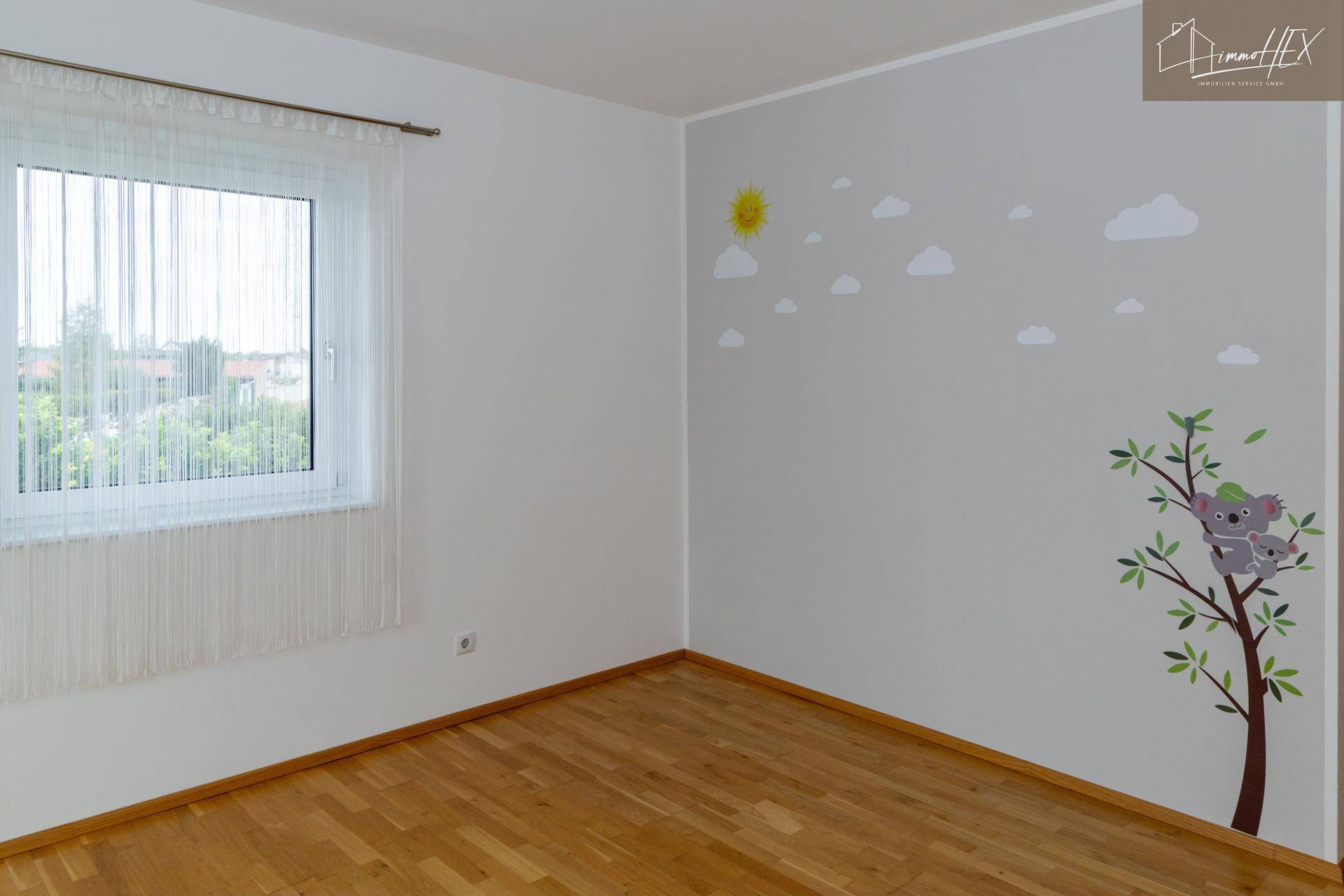 Kinderzimmer mit Holzboden, großem Fenster und Koala-Wandsticker.
