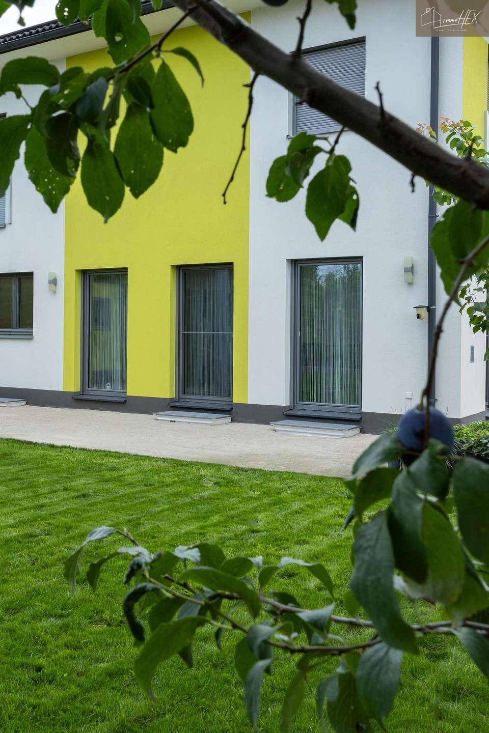 Blick auf die moderne Hausfassade mit gelben Akzenten und grüner Rasenfläche im Vordergrund.