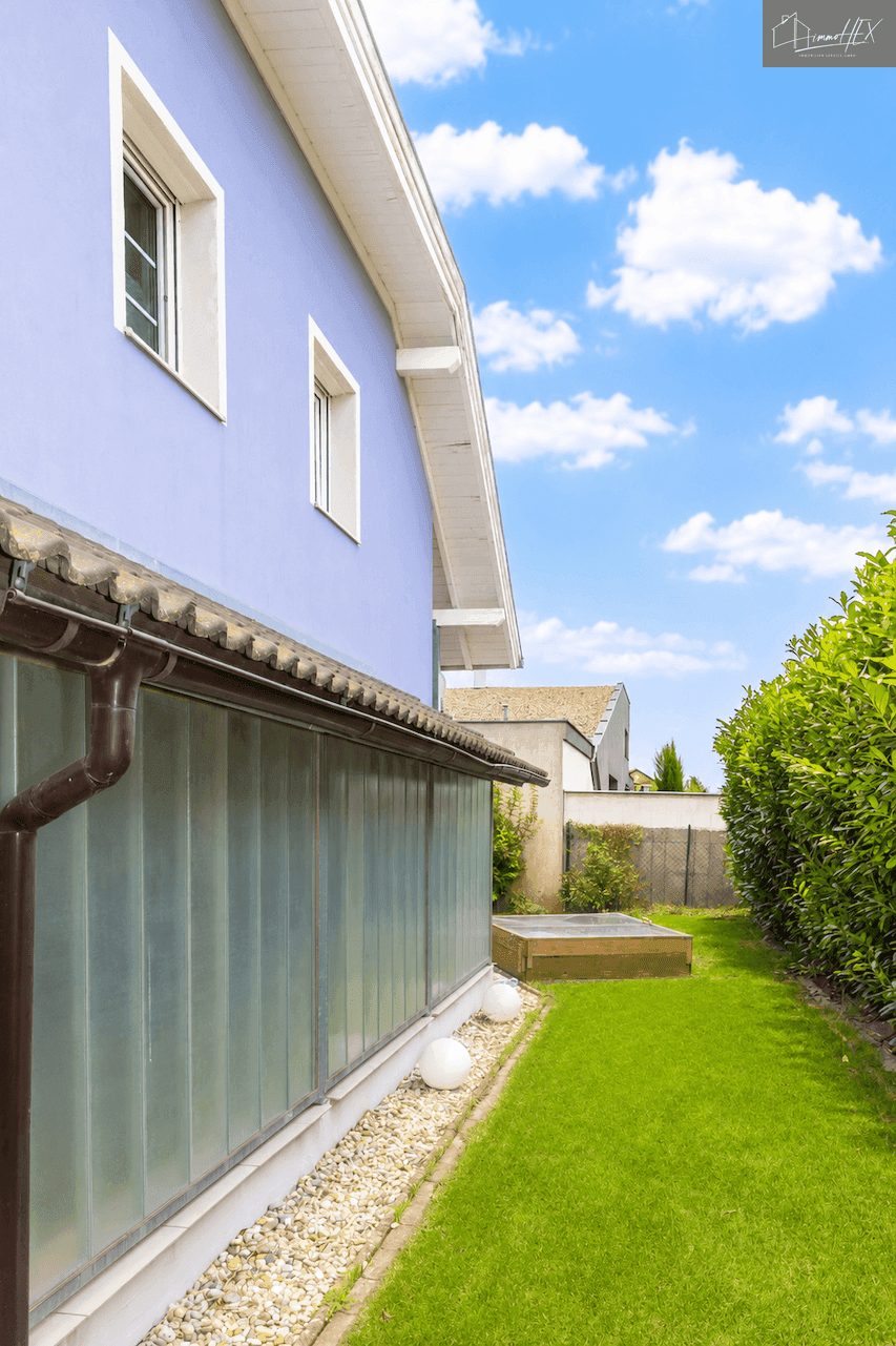 Seitenansicht des Hauses mit blauer Fassade, Fenstern und gepflegtem Garten.