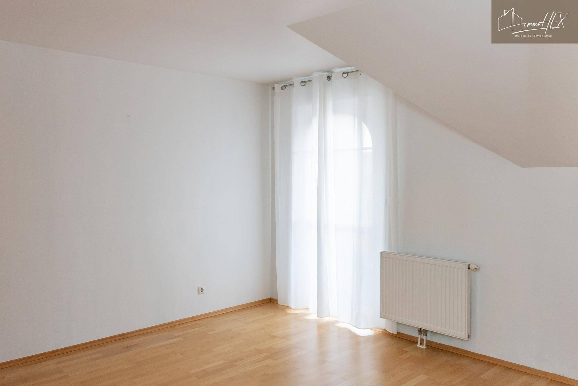 Helles Zimmer im Dachgeschoss mit Holzboden, Heizkörper und Dachschräge.