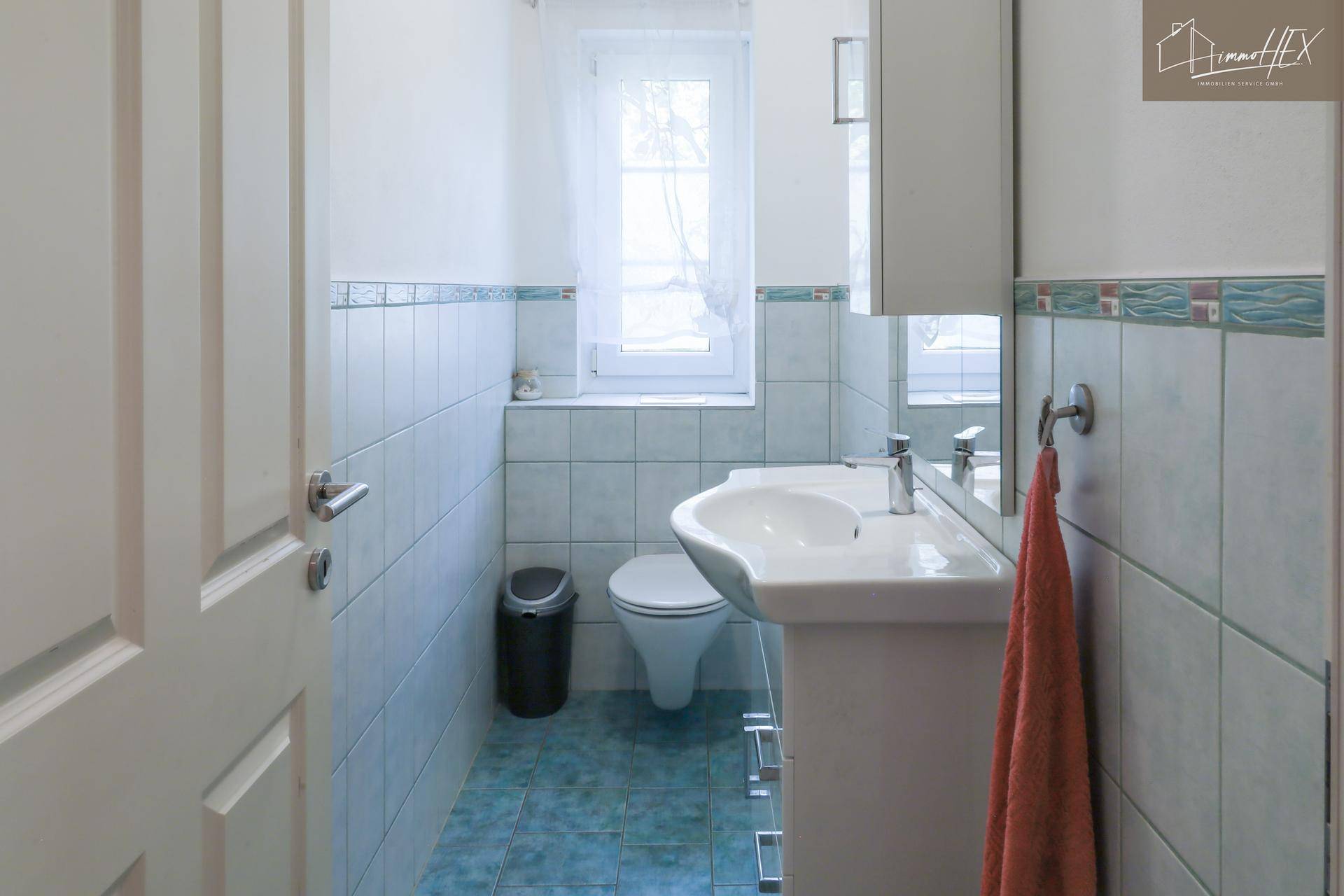 Badezimmer mit hellblauen Fliesen, Fenster und modernem Waschtisch mit Spiegel.
