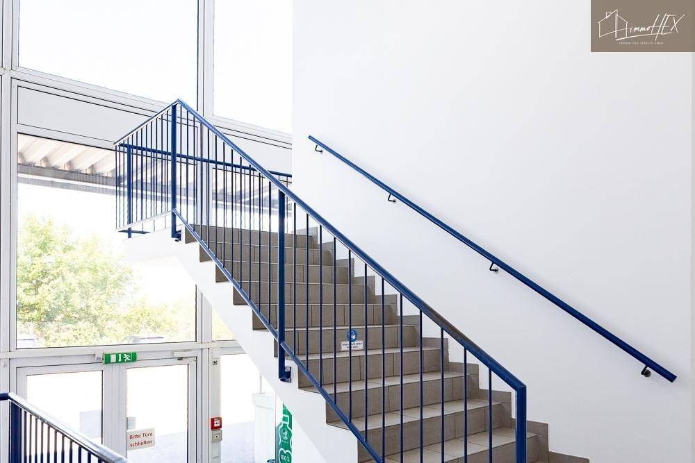 Detailansicht einer Treppe mit blauen Geländern und hellen Fliesenstufen.