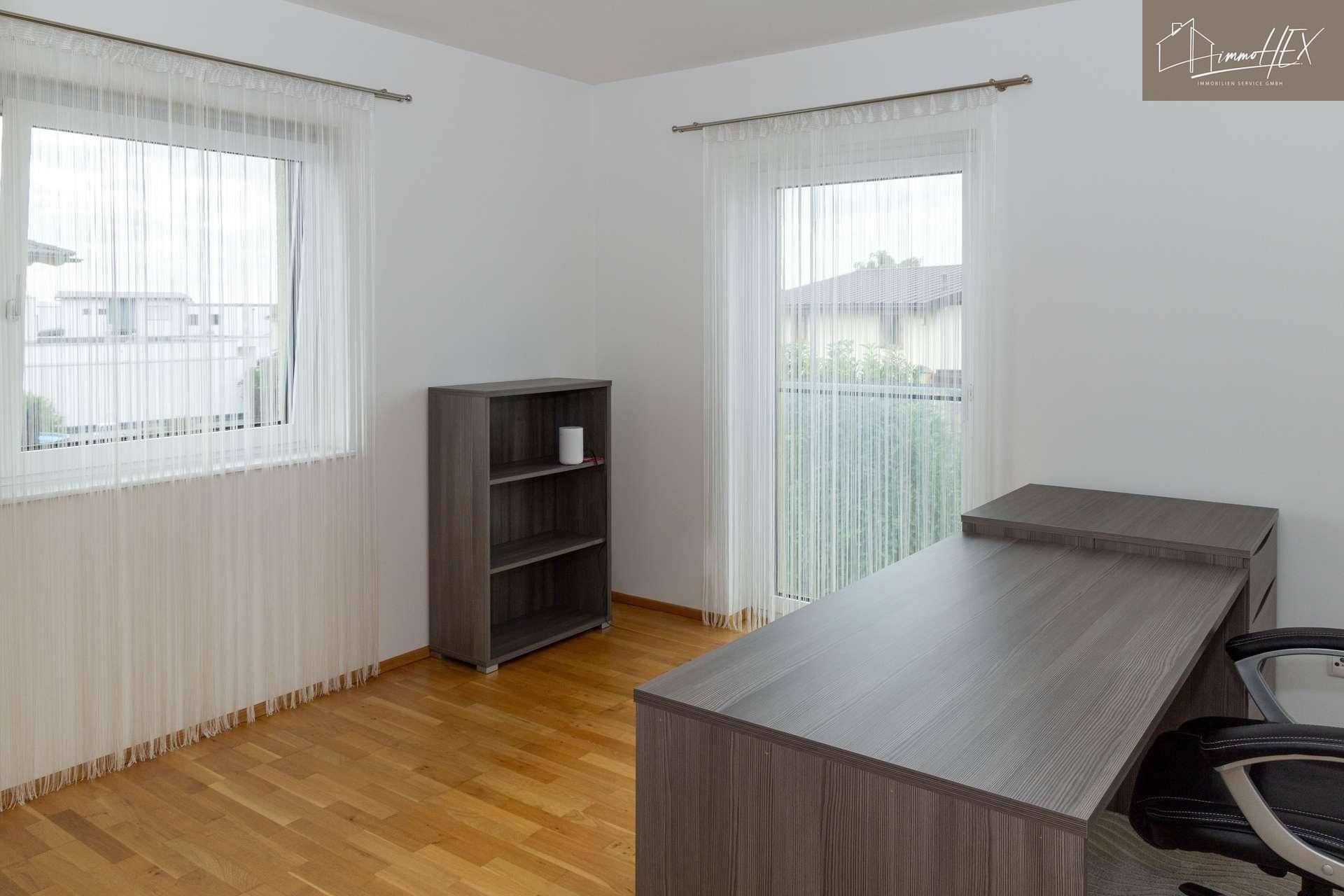 Helles Büro mit Holzboden, Schreibtisch und Fenster mit Blick ins Grüne.