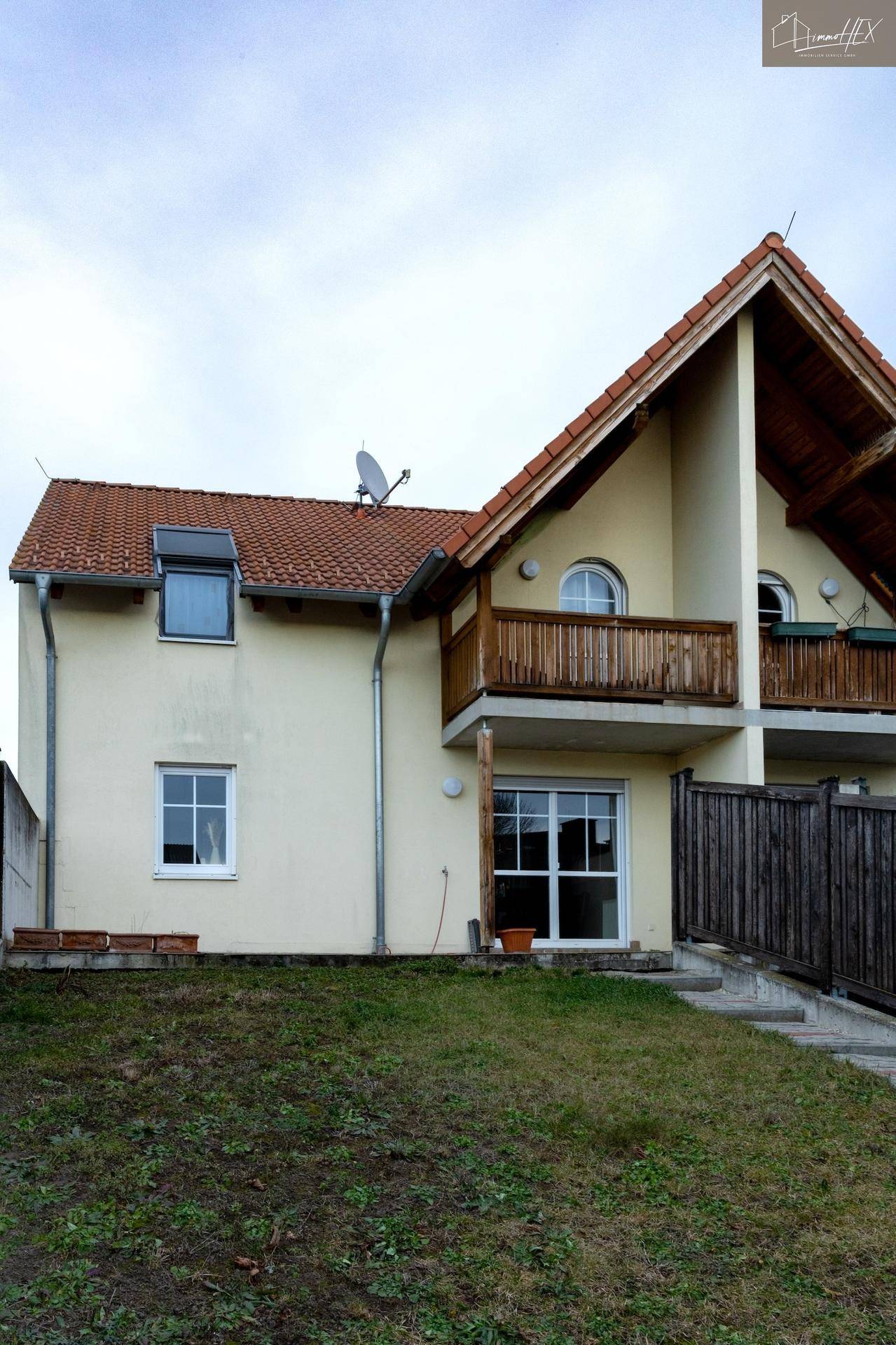 Ansicht des Hauses mit gelber Fassade, rotem Ziegeldach und Balkon.