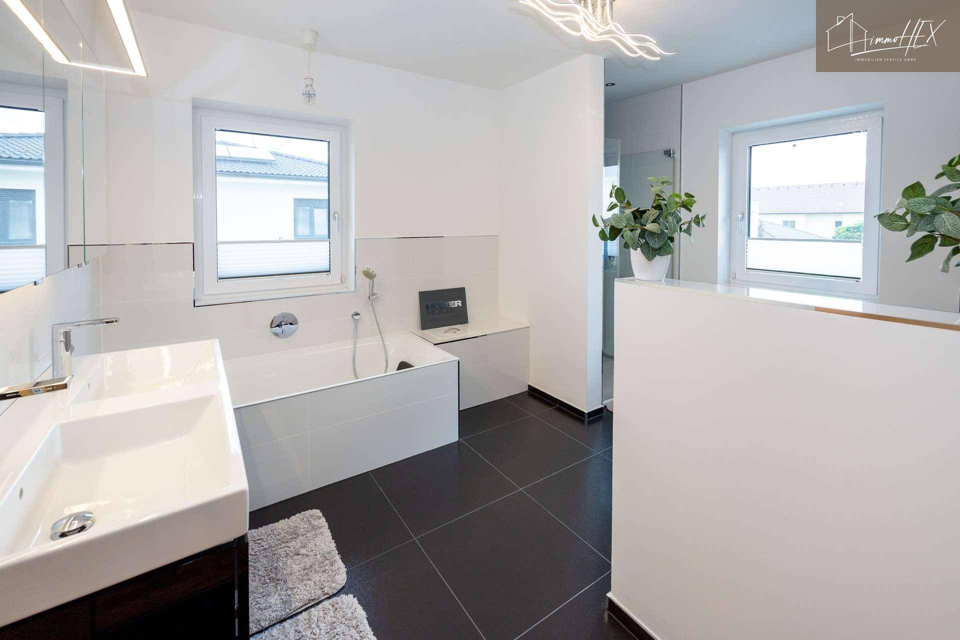 Modernes Badezimmer mit Badewanne, Doppelwaschbecken und dunklen Fliesen.