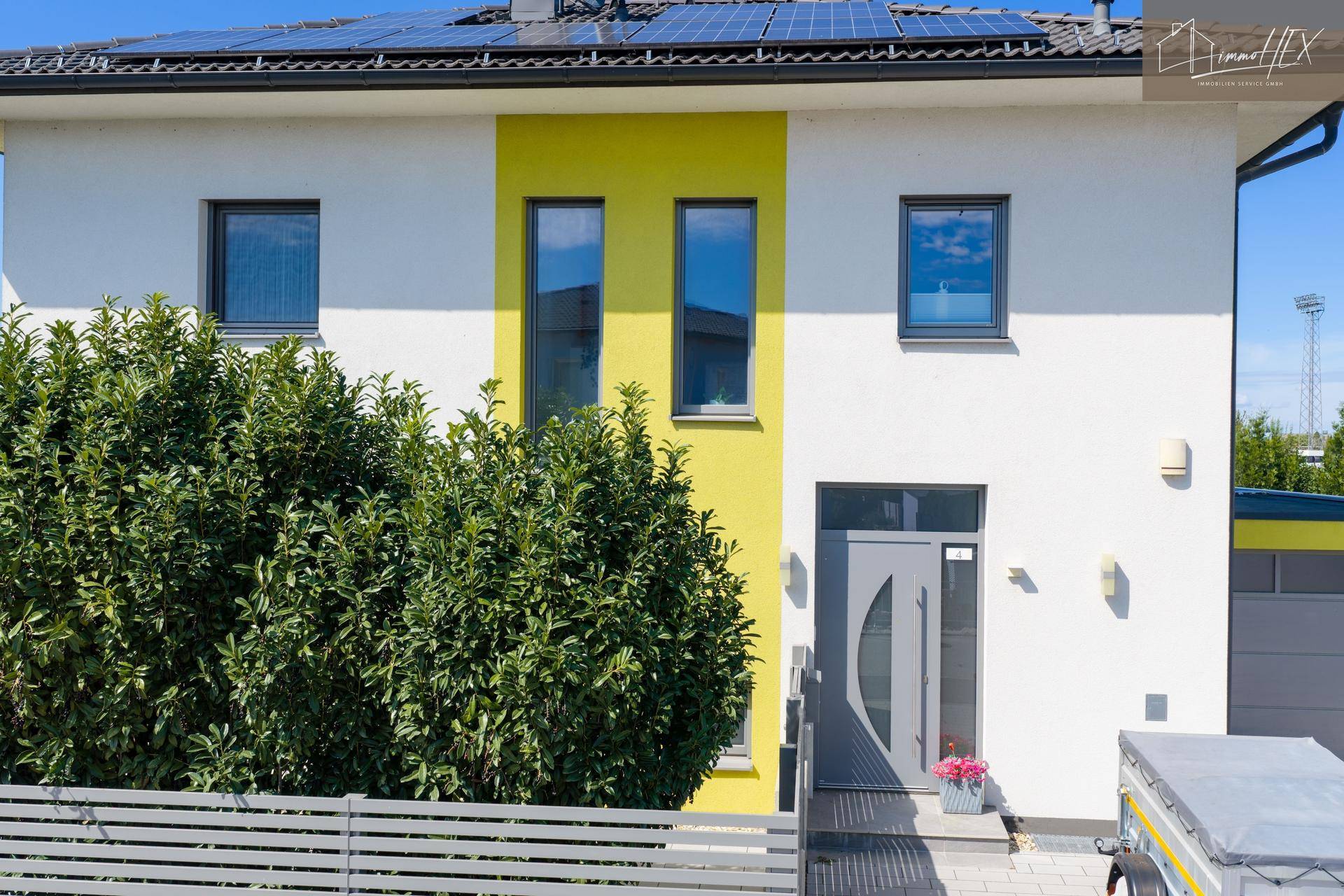 Nahaufnahme der modernen Hausfassade mit gelben Akzenten, Eingangsbereich und Solaranlage auf dem Dach.