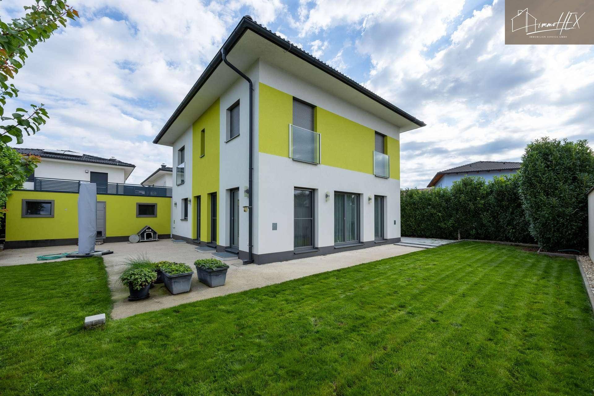 Modernes Einfamilienhaus mit gelben Akzenten, umgeben von einem gepflegten Garten und Terrasse.
