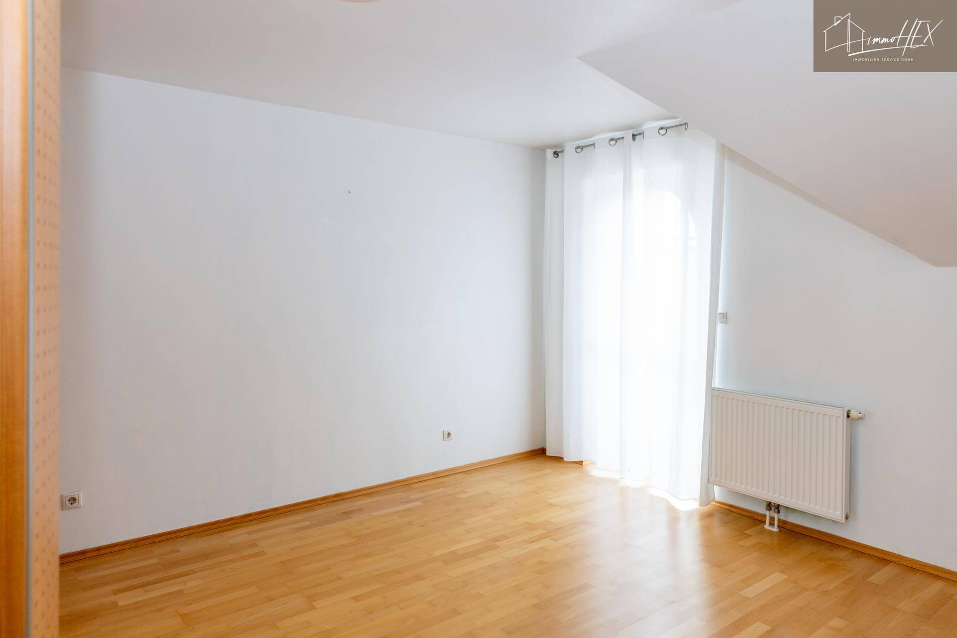 Geräumiges Zimmer im Dachgeschoss mit Holzboden, weiß gestrichenen Wänden und Dachschräge.