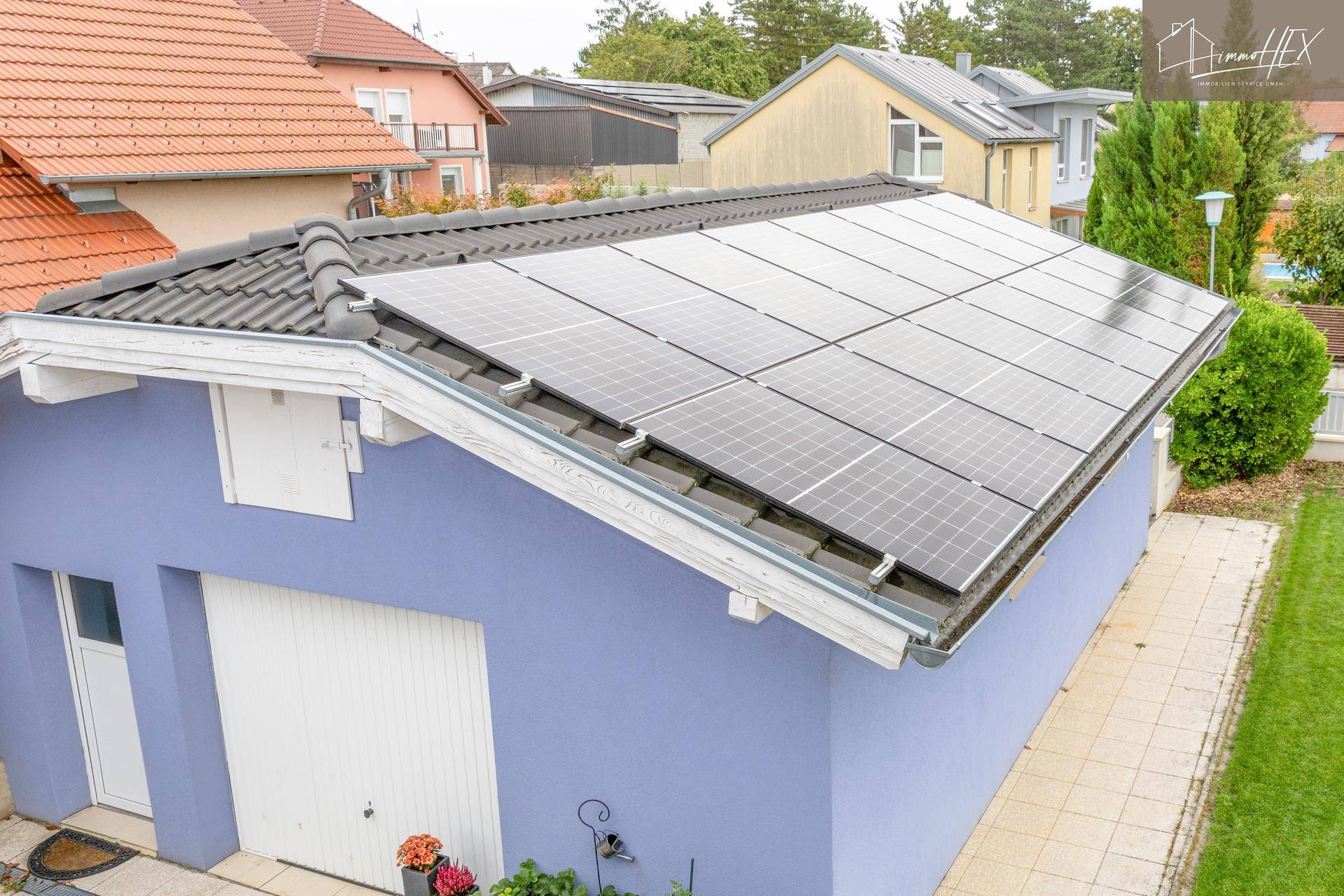 Garage mit Photovoltaikanlage auf dem Dach, umgeben von Wohnhäusern.