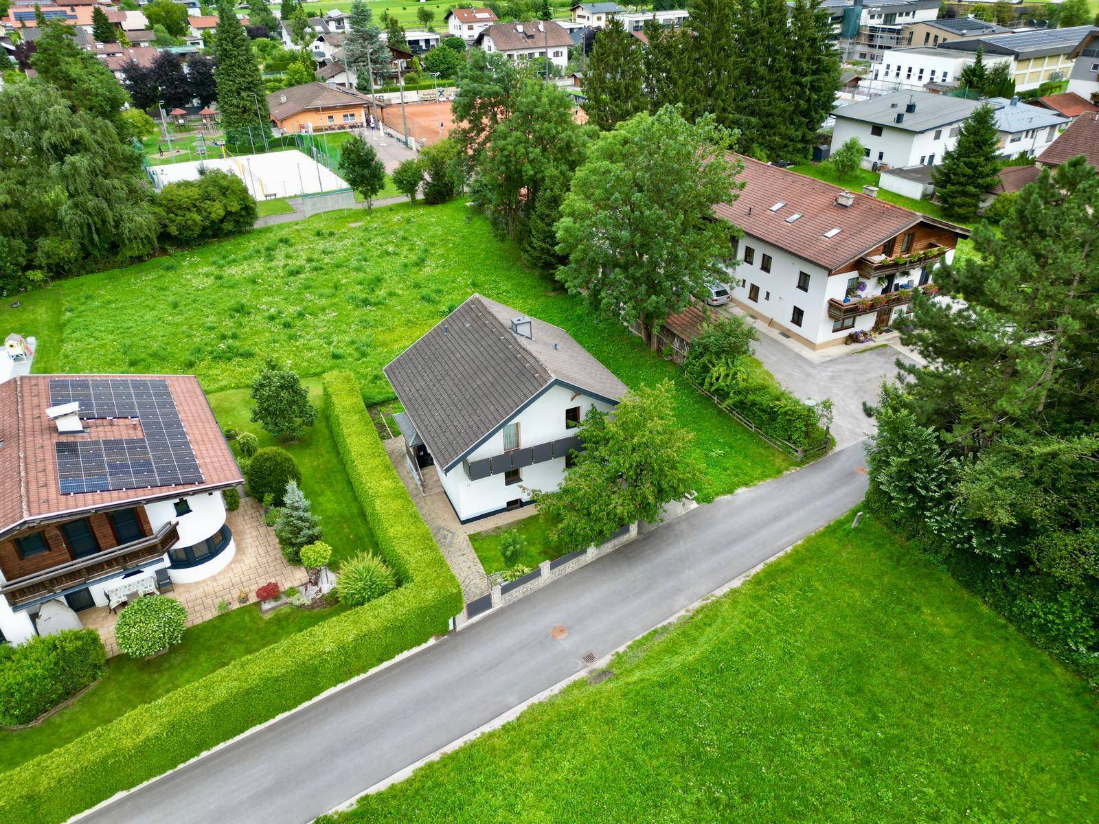 Luftaufnahme eines Einfamilienhauses in einer Wohnsiedlung mit viel Grün und Bergblick.