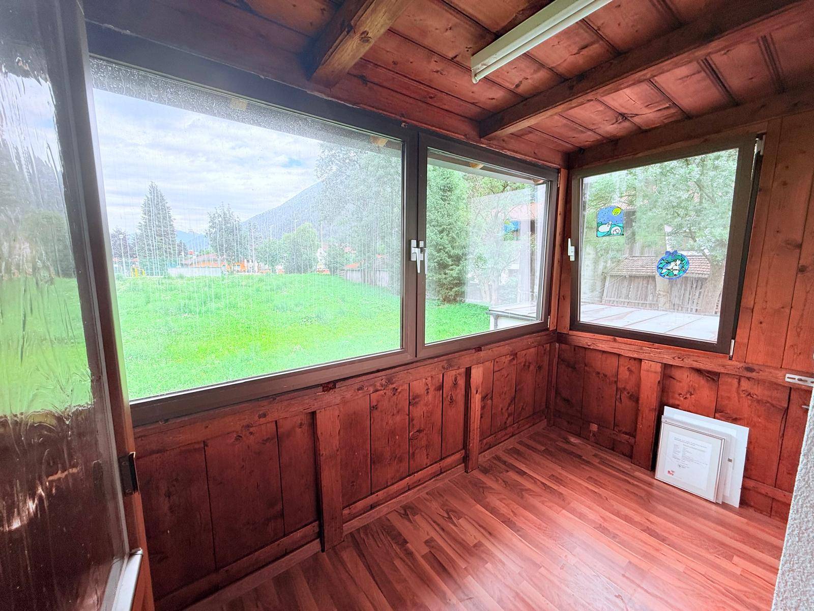 Verglaster Wintergarten mit Holzverkleidung, Holzboden und weitem Blick ins Grüne.