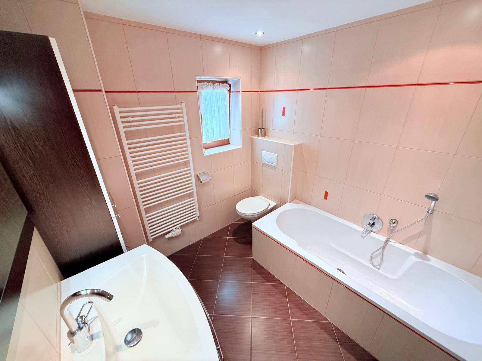 Badezimmer mit Badewanne, WC, beheiztem Handtuchhalter und Fenster.