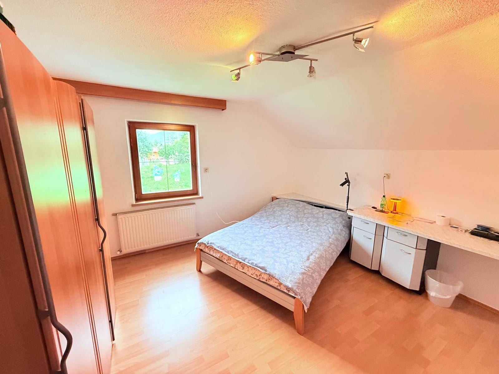 Schlafzimmer mit Holzboden, Dachschräge und Fenster mit Blick ins Grüne.