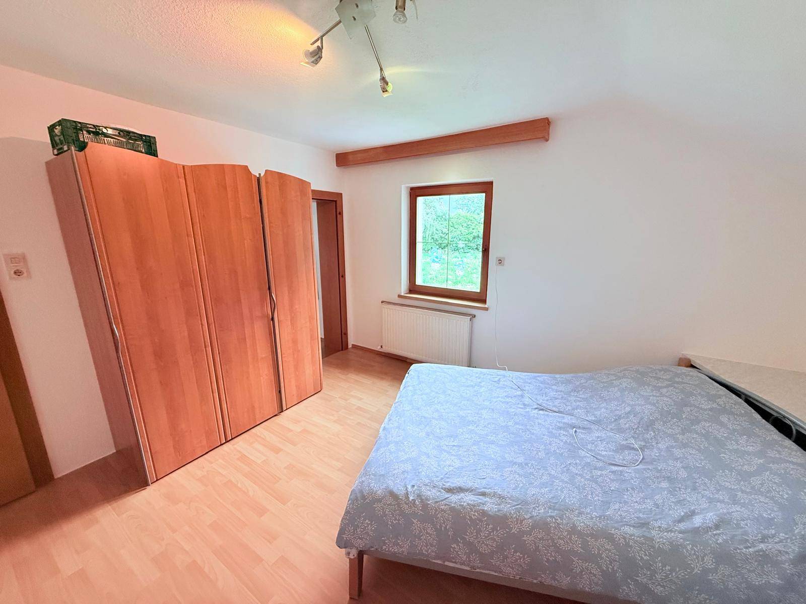 Helles Schlafzimmer mit Holzboden, großem Kleiderschrank und Fenster.