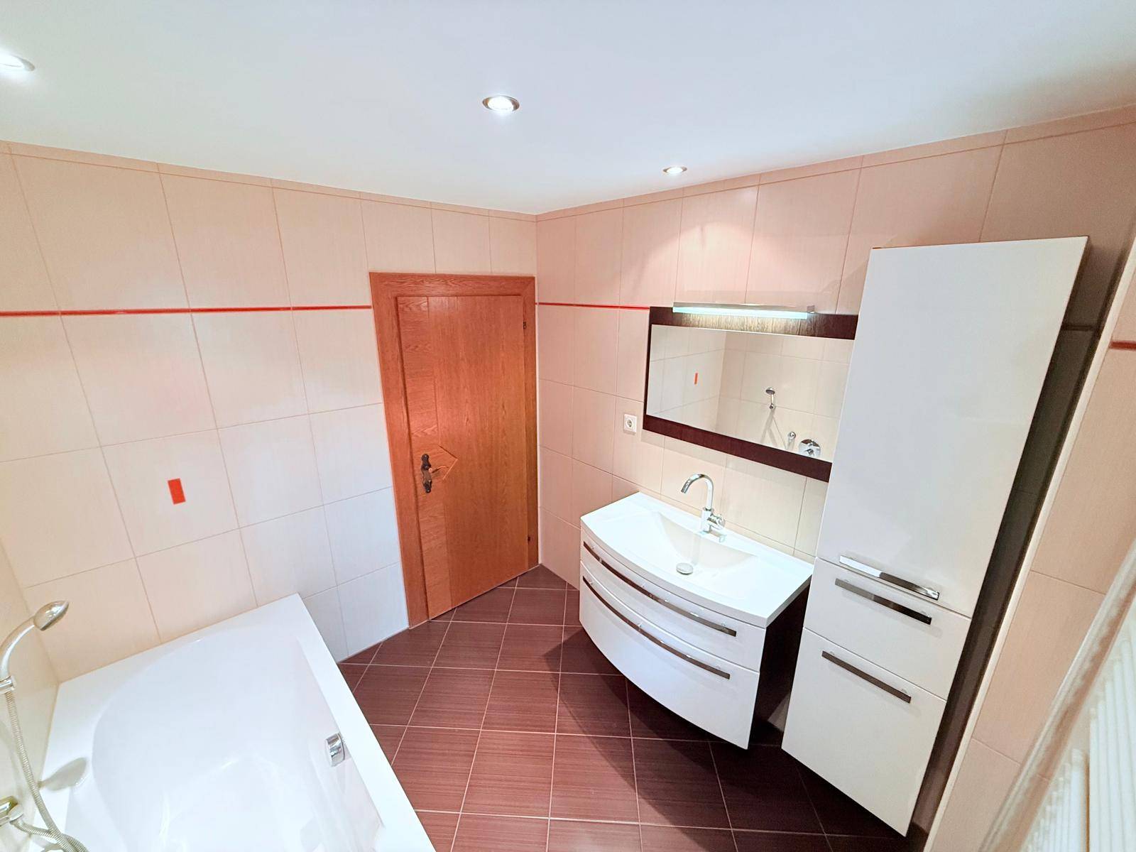 Modernes Badezimmer mit Badewanne, Waschtisch und hellen Fliesen.