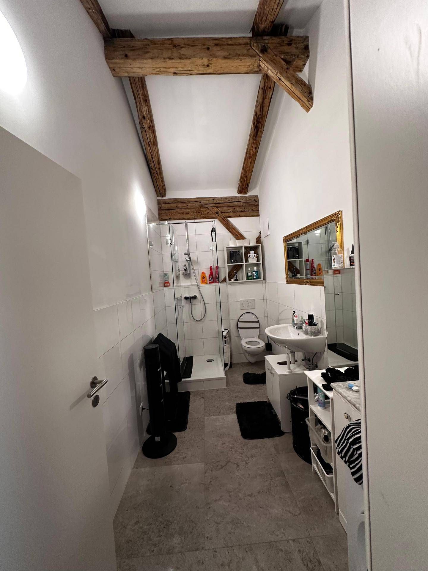 Funktionales Badezimmer mit Dusche, Waschbecken, WC und rustikalen Holzbalken unter der Dachschräge.