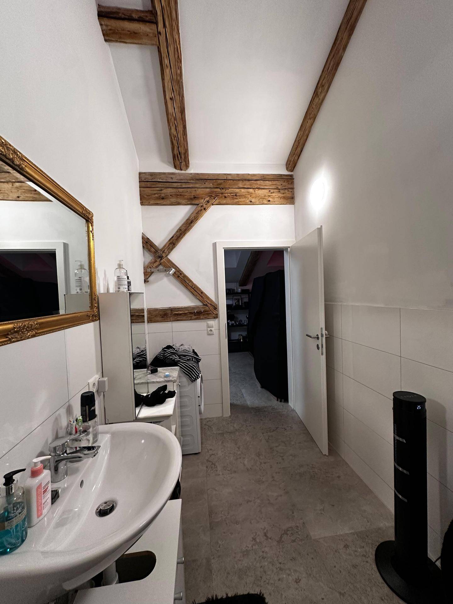 Badezimmer mit Waschbecken, großem Spiegel und sichtbaren Holzbalken, die den Raum charakterisieren.