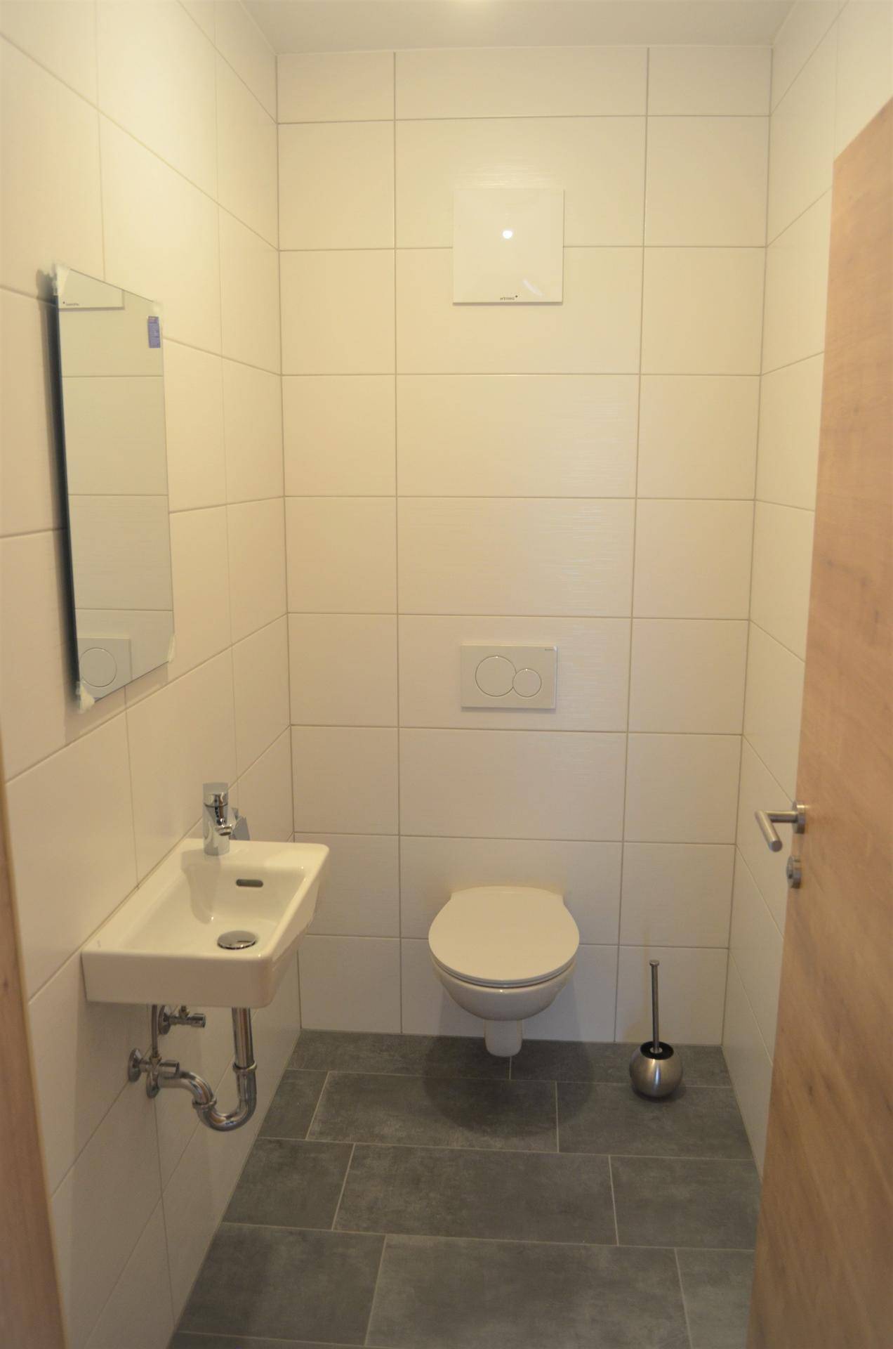Modernes Gäste-WC mit Wand-WC, kleinem Waschbecken und hellen Fliesen.