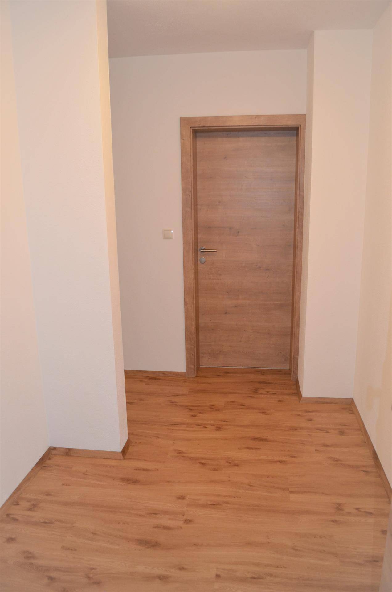 Heller Flur mit Holztür und Laminatboden, der zu weiteren Räumen führt.