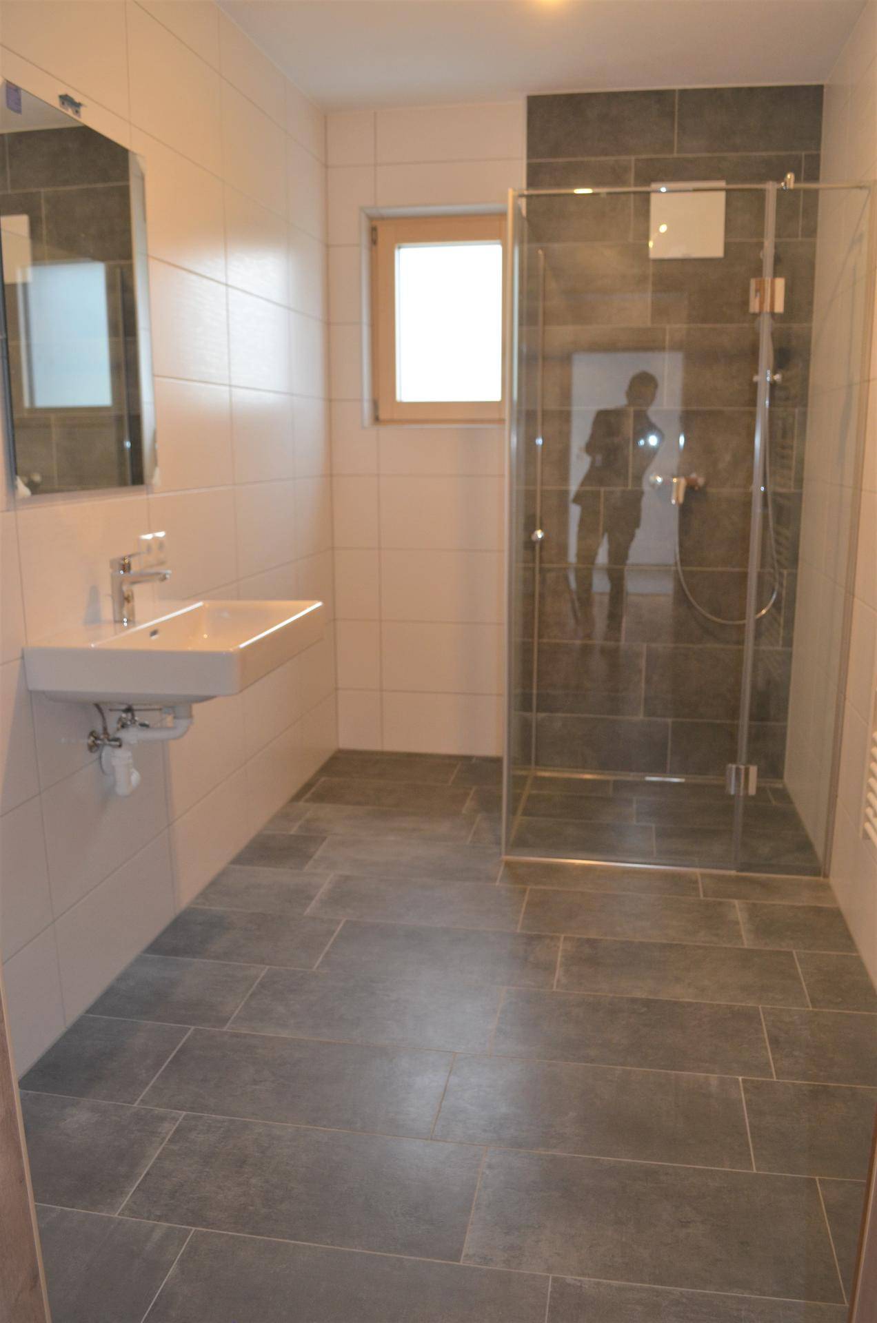 Helles Badezimmer mit ebenerdiger Dusche, Waschbecken und Fenster.