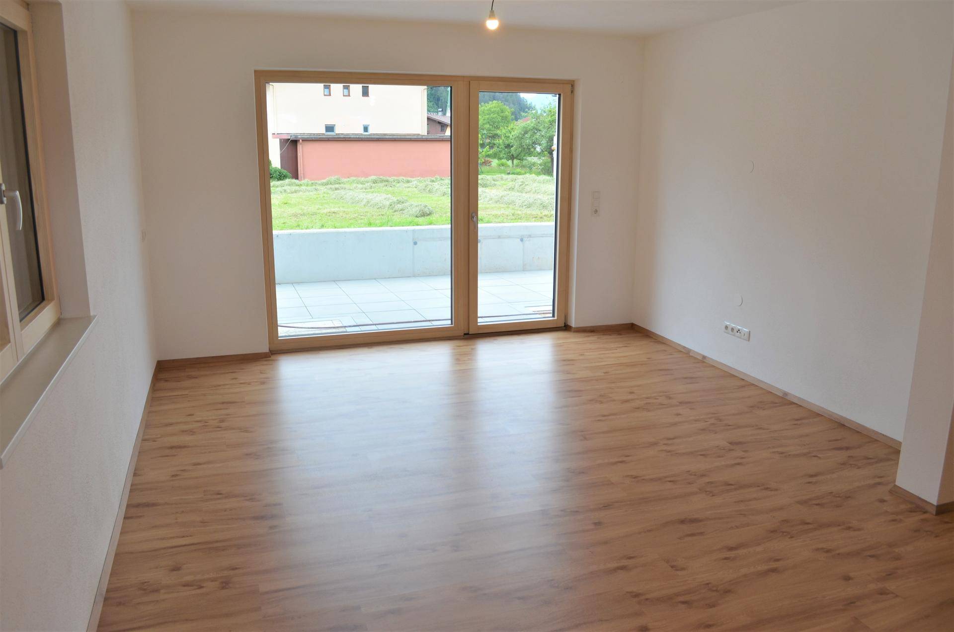 Heller, leerer Wohnbereich mit großen Terrassentüren und Blick ins Grüne.