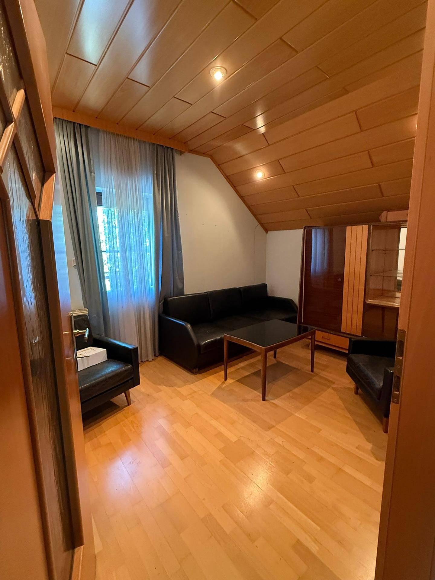 Wohnzimmer mit schwarzem Sofa, Holzboden und Holzdecke, bietet eine gemütliche Atmosphäre.