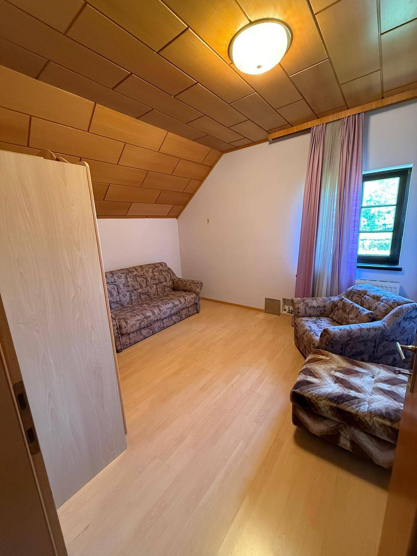 Gemütlicher Wohnbereich mit gemusterten Sitzmöbeln, Holzboden und Holzdecke unter einer Dachschräge.
