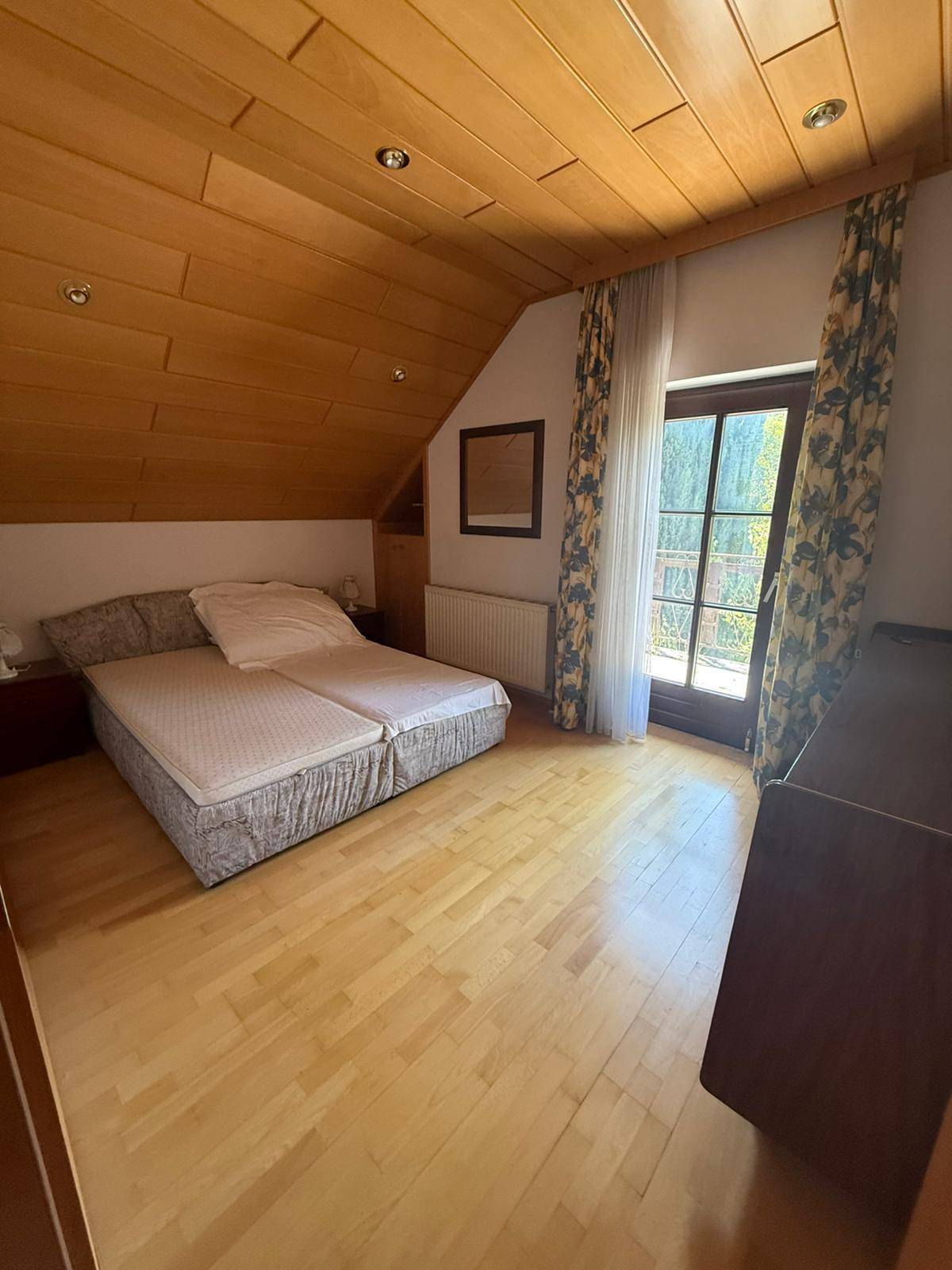 Dachschlafzimmer mit Holzdecke, Holzboden und Zugang zu einem Balkon, hell und geräumig.