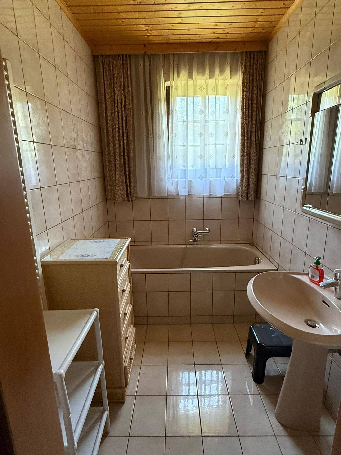 Badezimmer mit beigefarbenen Fliesen, Badewanne, Waschbecken und Fenster, im traditionellen Stil.