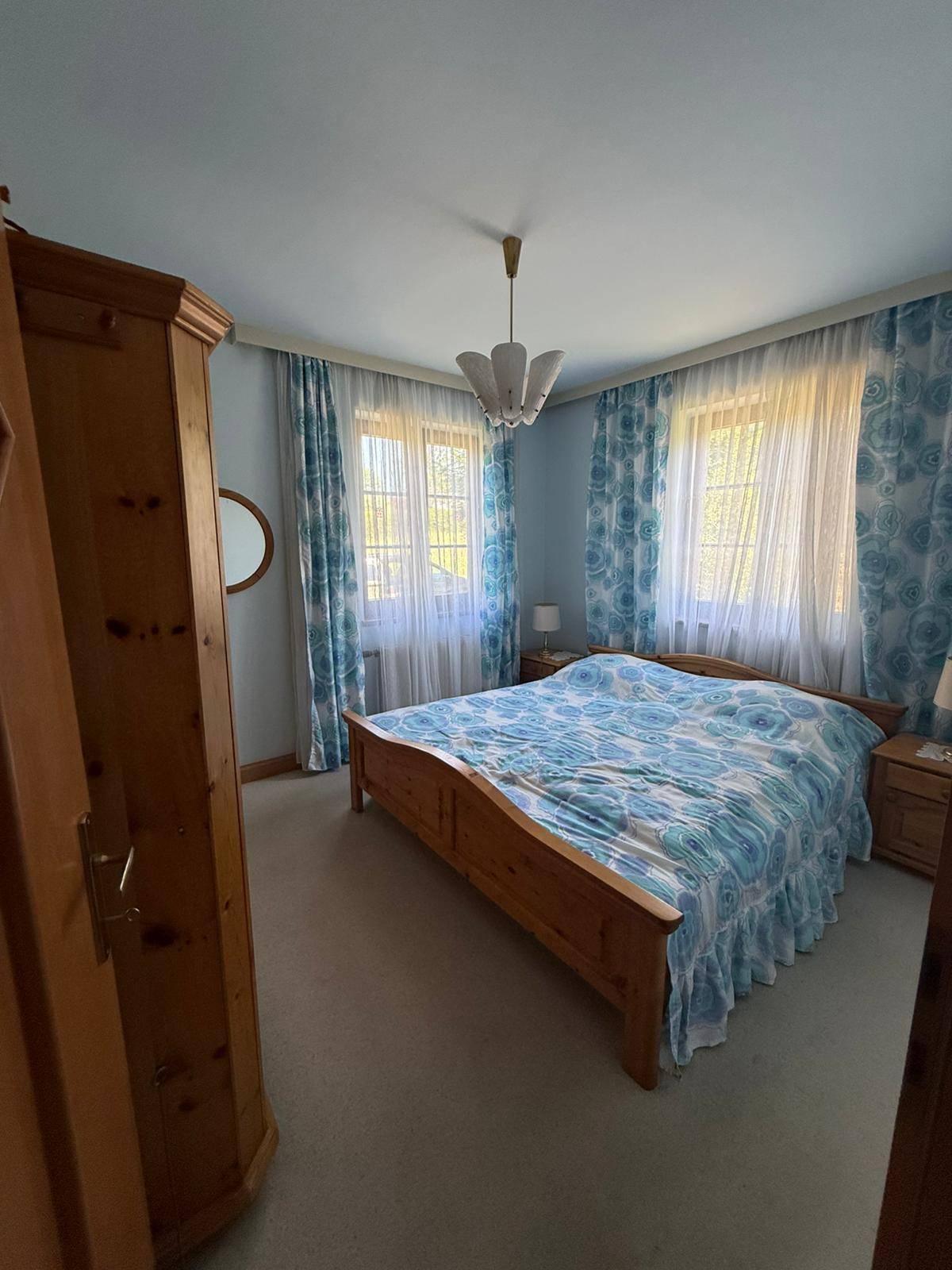 Schlafzimmer mit Holzmöbeln, blauen Vorhängen und Teppichboden, bietet eine ruhige Atmosphäre.