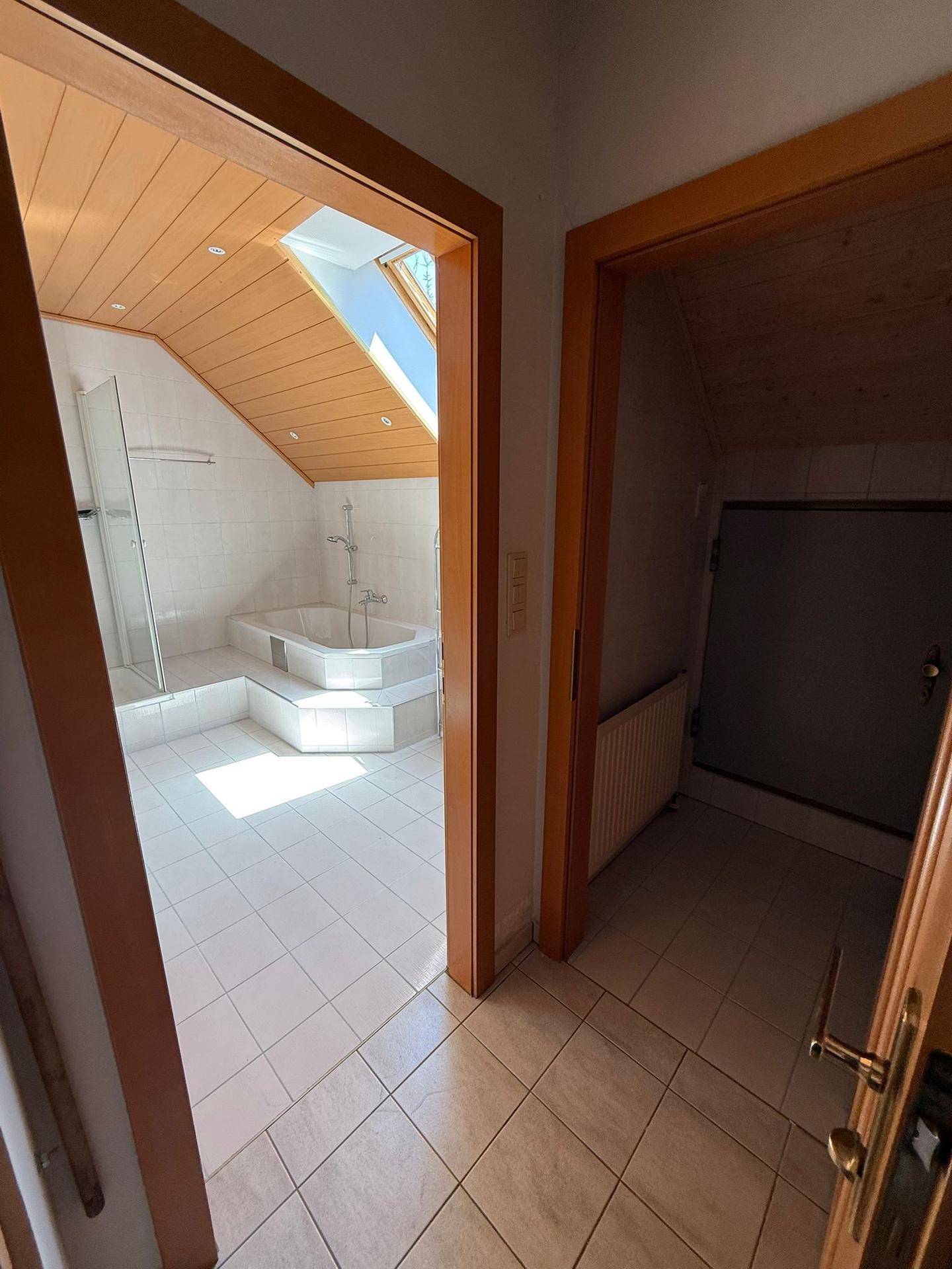 Badezimmer mit Eckbadewanne, Dusche und Dachschräge, durch eine Tür vom Flur aus sichtbar.