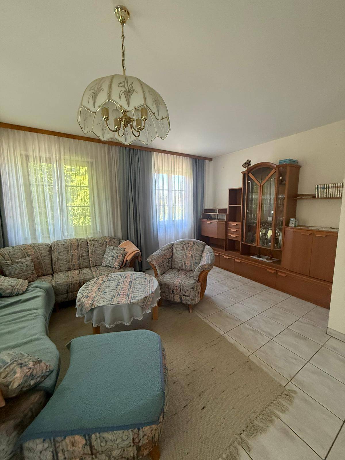 Gemütliches Wohnzimmer mit gemusterten Möbeln, einem großen Holzschrank und Fliesenboden mit Teppich.