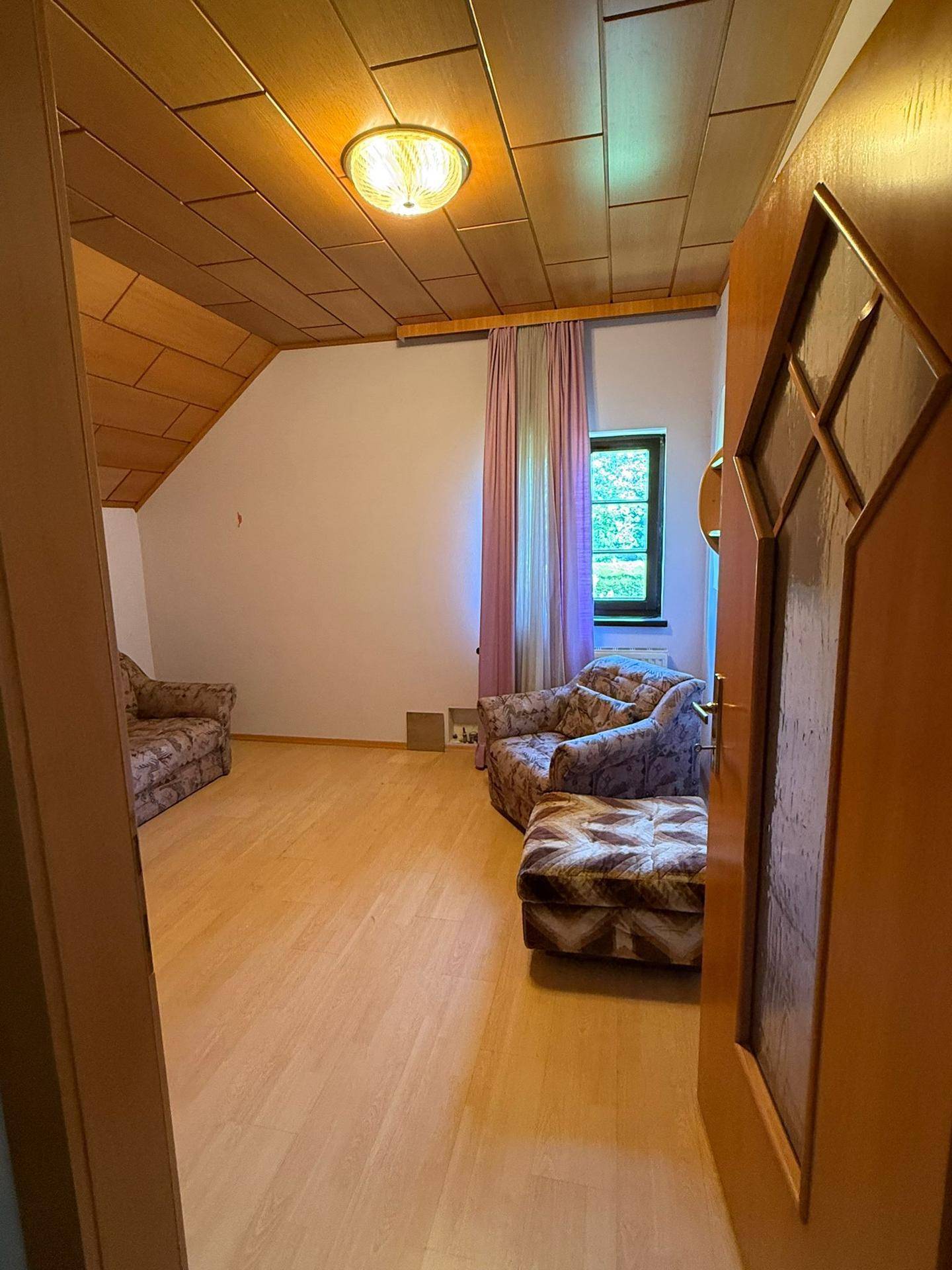 Heller Wohnbereich mit Holzboden und Holzdecke, gemusterten Möbeln und einer Tür im Vordergrund.