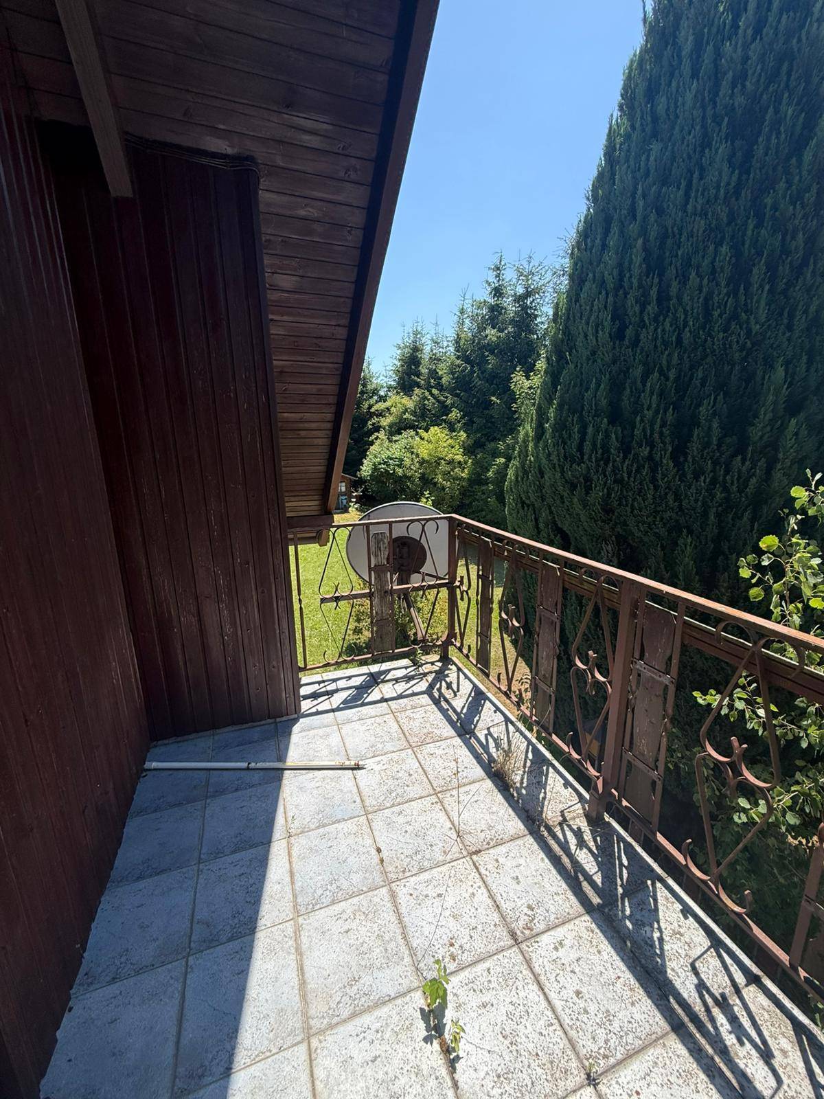 Kleiner Balkon mit Fliesenboden und altem Metallgeländer, bietet einen Blick ins Grüne.