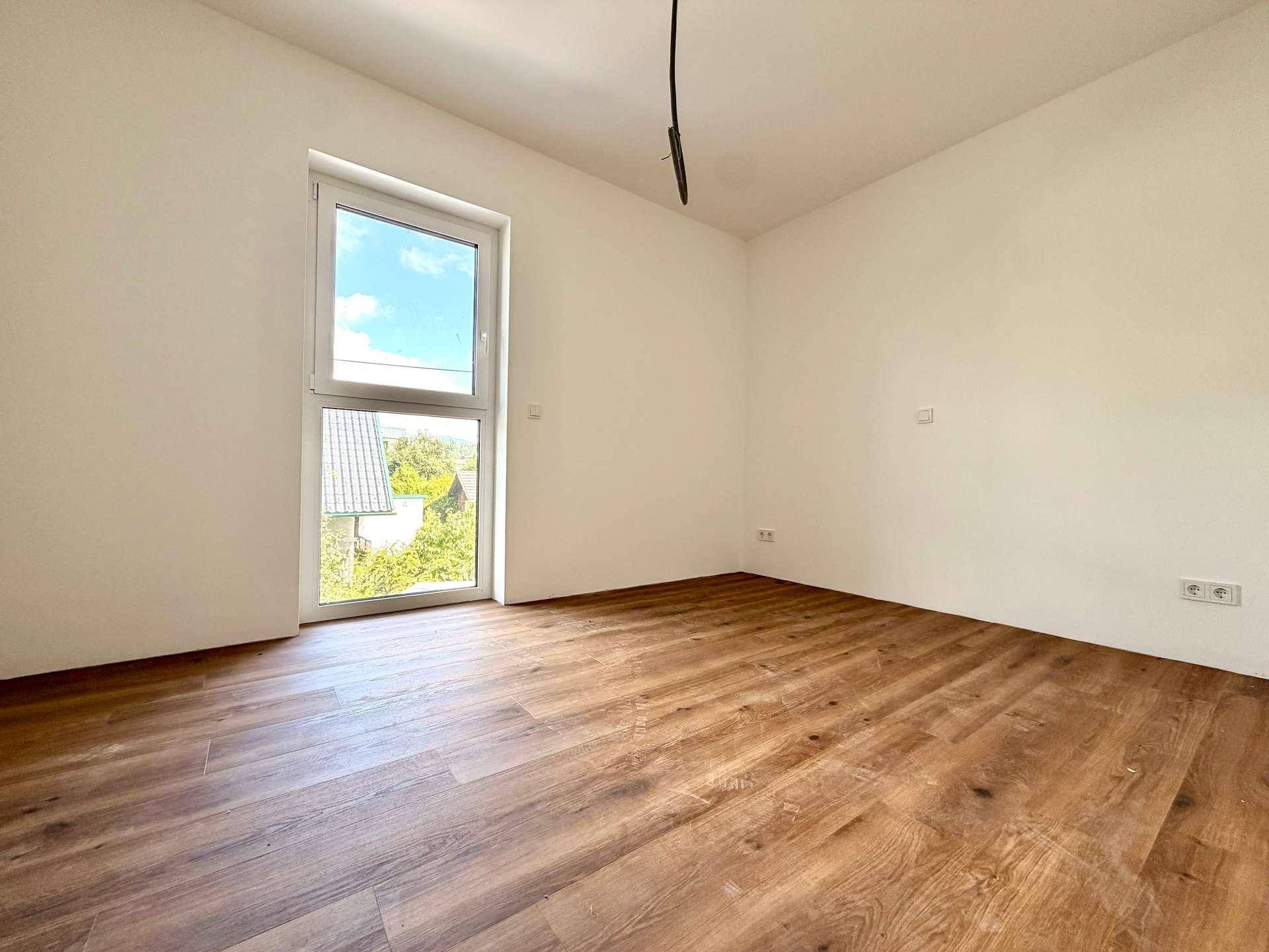Leerer Raum mit Laminatboden und einem Fenster, das viel Tageslicht hereinlässt.
