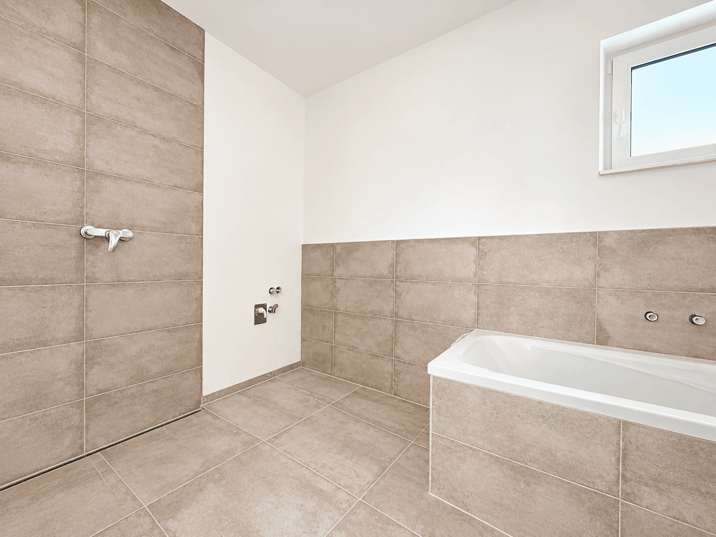 Badezimmer im Rohbau mit Fliesenboden und Badewanne, bereit für die Fertigstellung.